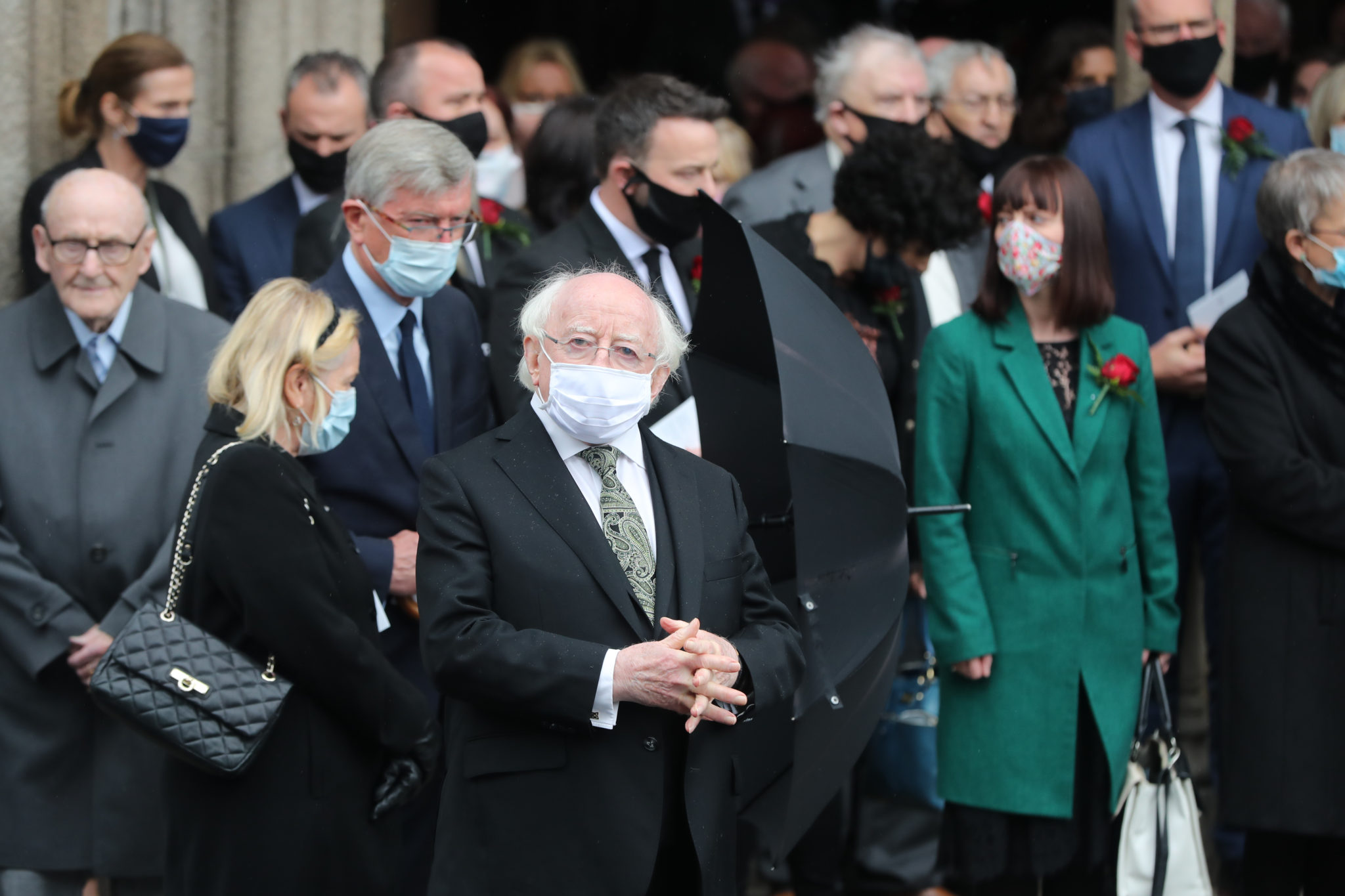 he President Michael D Higgins stands with mourners following the funeral service of John Hume