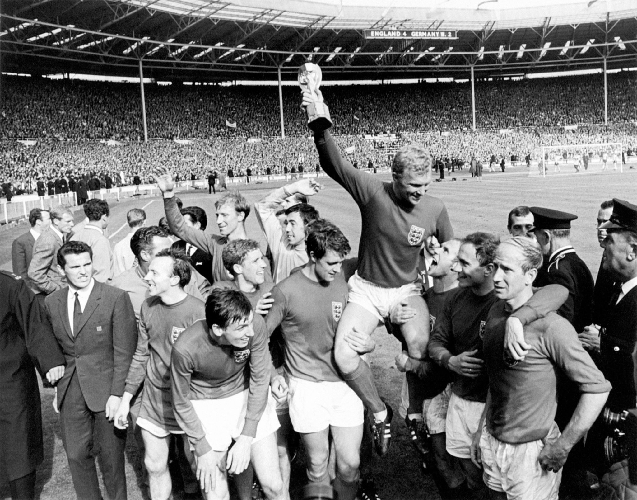 England captain Bobby Moore holds the World Cup aloft as he is chaired by his jubilant teammates: (l-r) Nobby Stiles, Martin Peters (front), Jack Charlton (back), Alan Ball, Gordon Banks, Geoff Hurst, Roger Hunt (hidden behind Hurst), Bobby Moore, Ray Wilson, George Cohen, Bobby Charlton. Other members of the England squad in the picture are Jimmy Greaves (background, far l), Ron Flowers (background, second l), Terry Paine (l of Stiles), Gerry Byrne (behind Bobby Charlton's head)