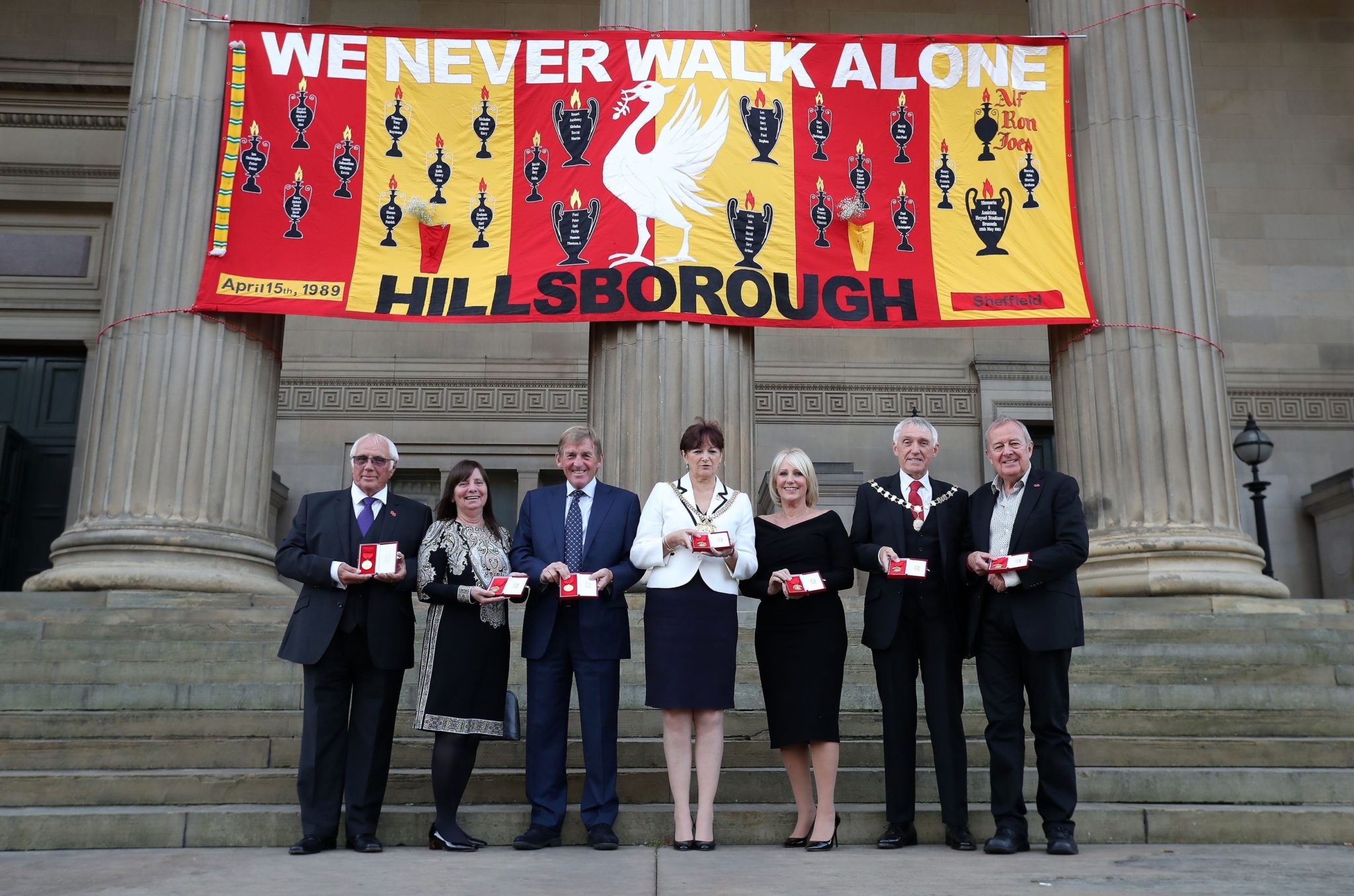 Trevor Hicks, Margaret Apsinall, Kenny Dalglish, the Lord Mayor of Liverpool Roz Gladden, Marina Dalglish, Consort Roy Gladden and Professor Phil Scraton all hold a medal for each of the 96 victims of the Hillsborough disaster at Liverpool Town Hall.