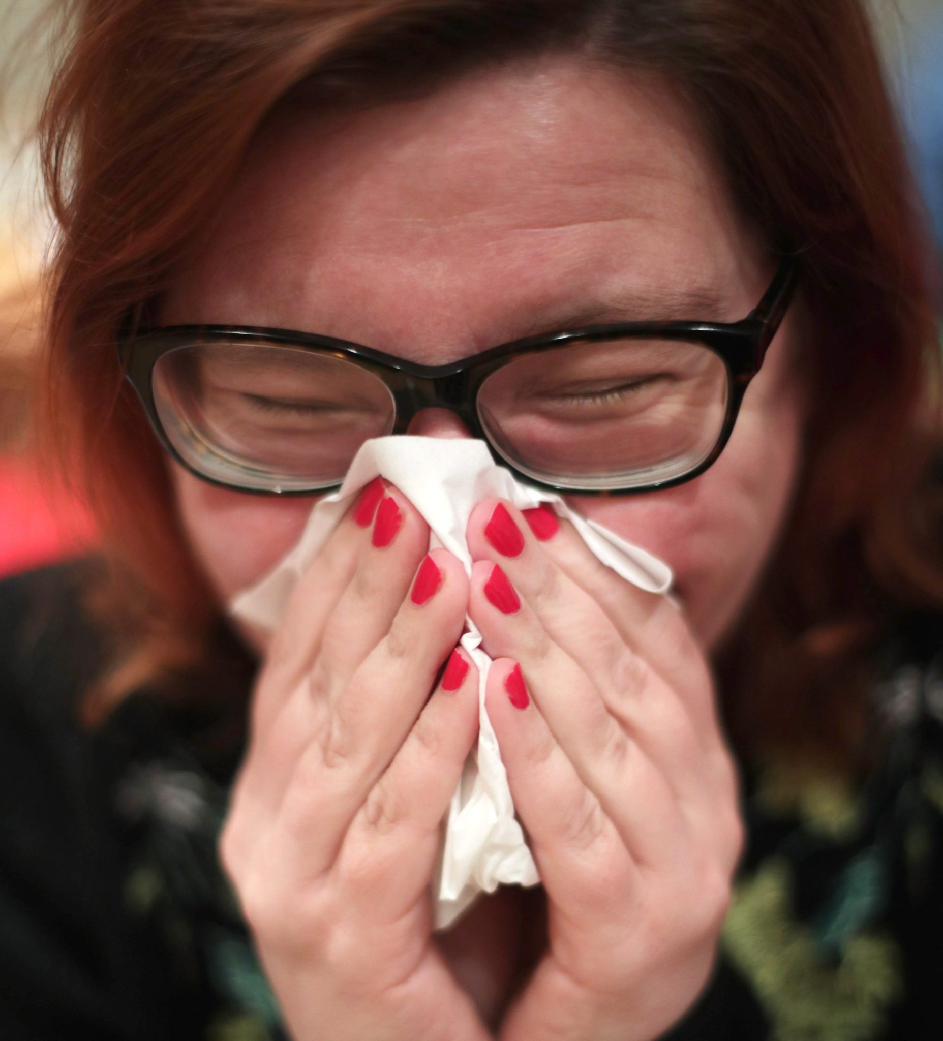 A woman with a cold blowing her nose with a tissue.