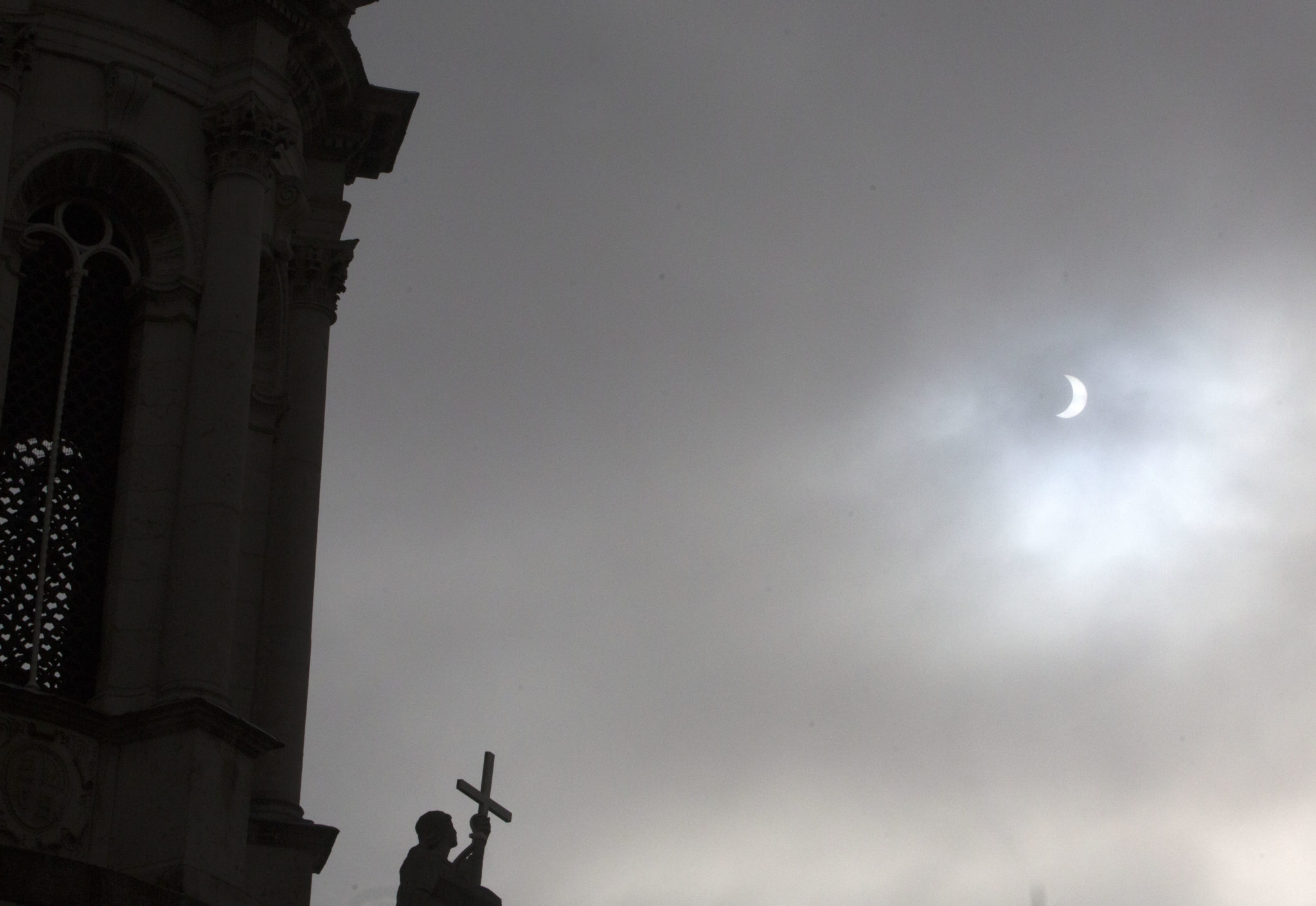 A partial solar eclipse appears briefly through the clouds beside the Campanile in Trinity College Dublin