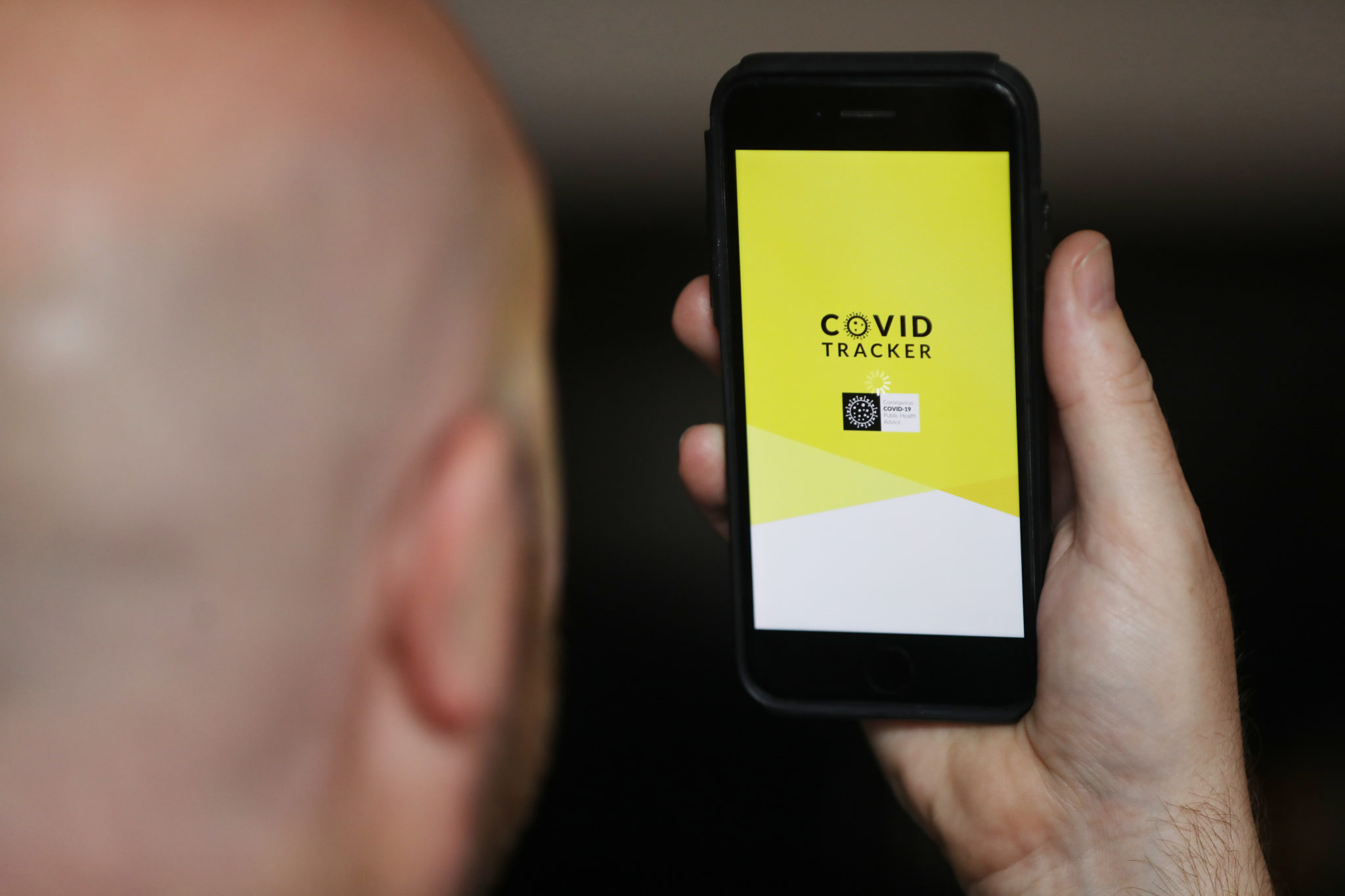 A man holds a phone running the COVID Tracker app
