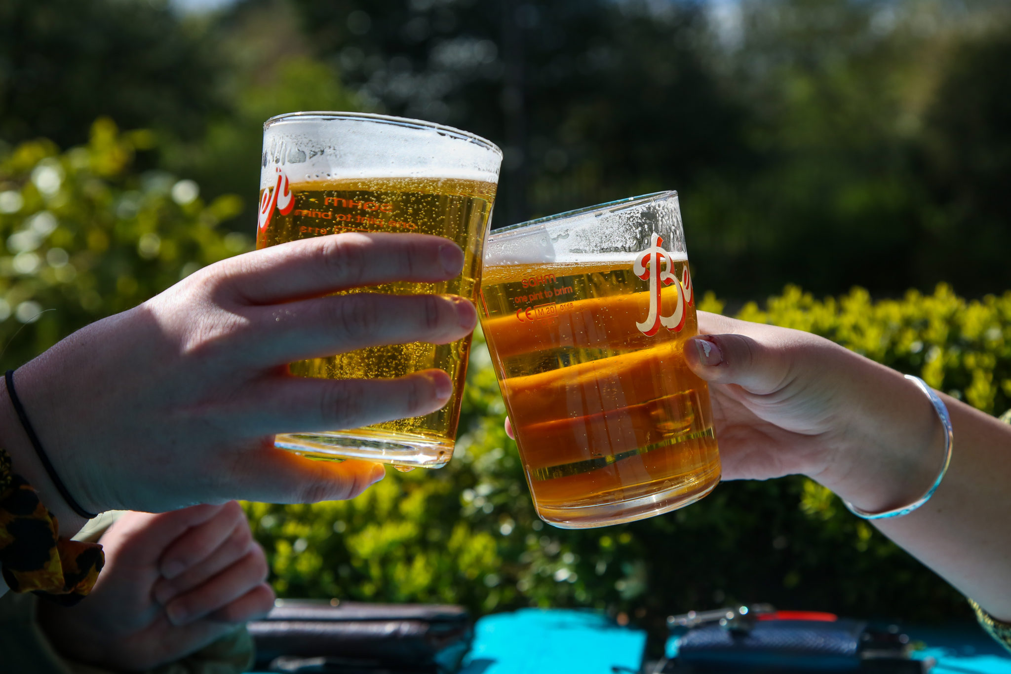 A couple raises their pints of beer on a warm sunny morning in a beer garden of a pub in London.