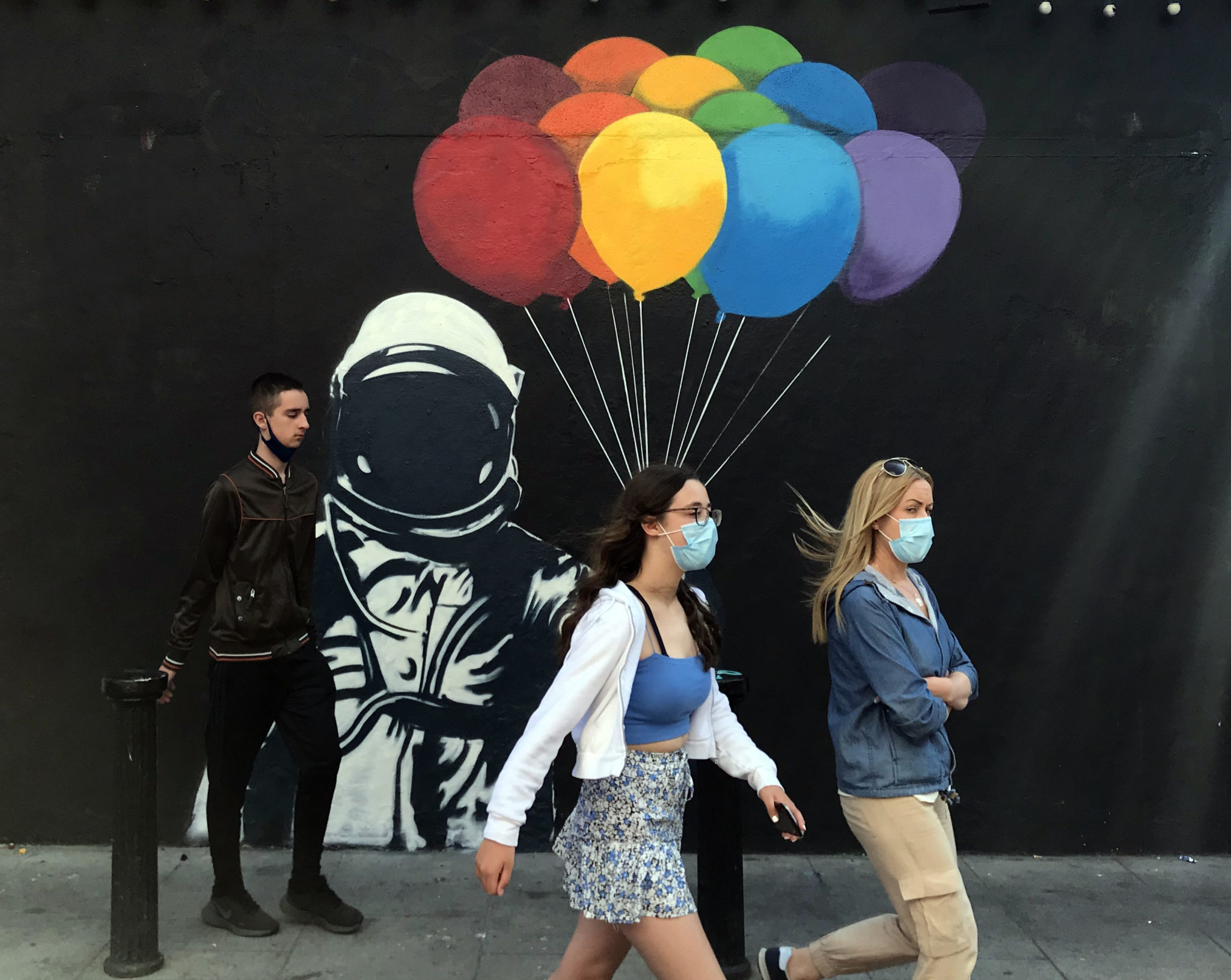 Two women wearing face masks walk past a spaceman with balloons mural in Dublin