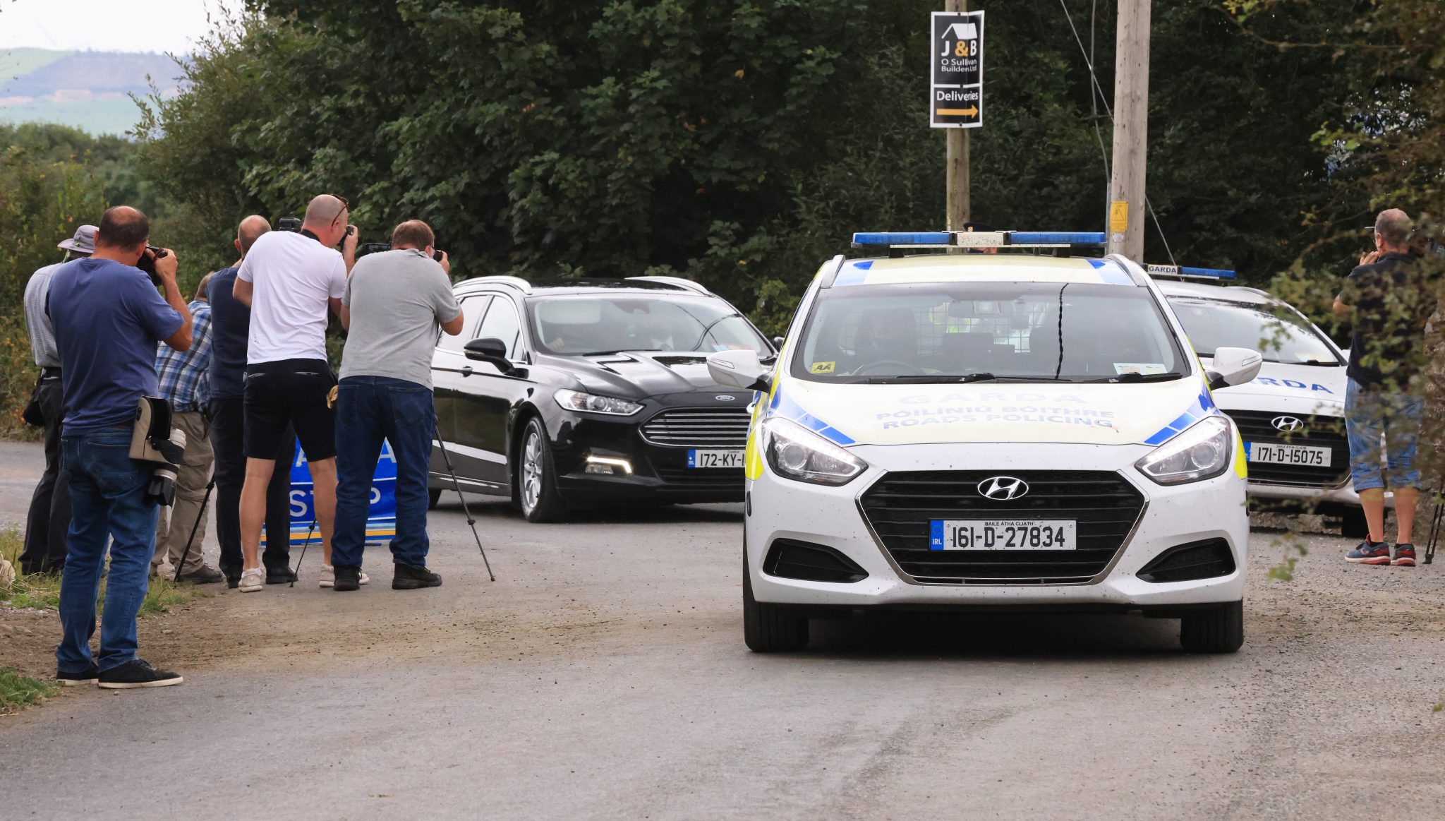Garda cars escort cars carrying the bodies of three people past waiting media and away from the scene on the approach road to Ballyreehan, Lixnaw in Co Kerry.