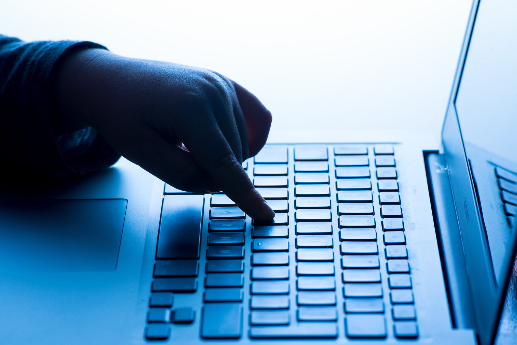 Person with fingers on keyboard of laptop in dark lighting