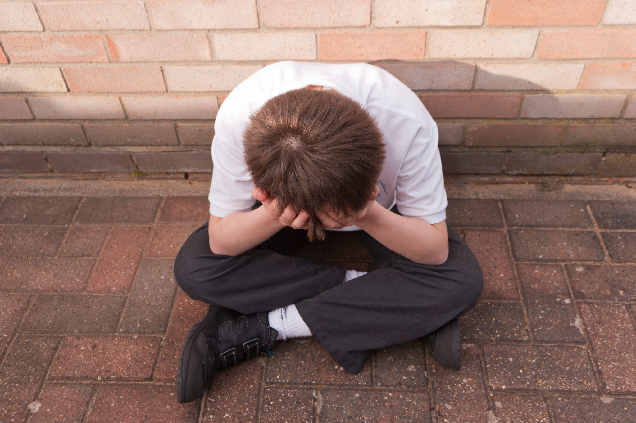 A young boy looking depressed outdoors wearing his school uniform. Image: T.M.O.Pictures / Alamy Stock Photo