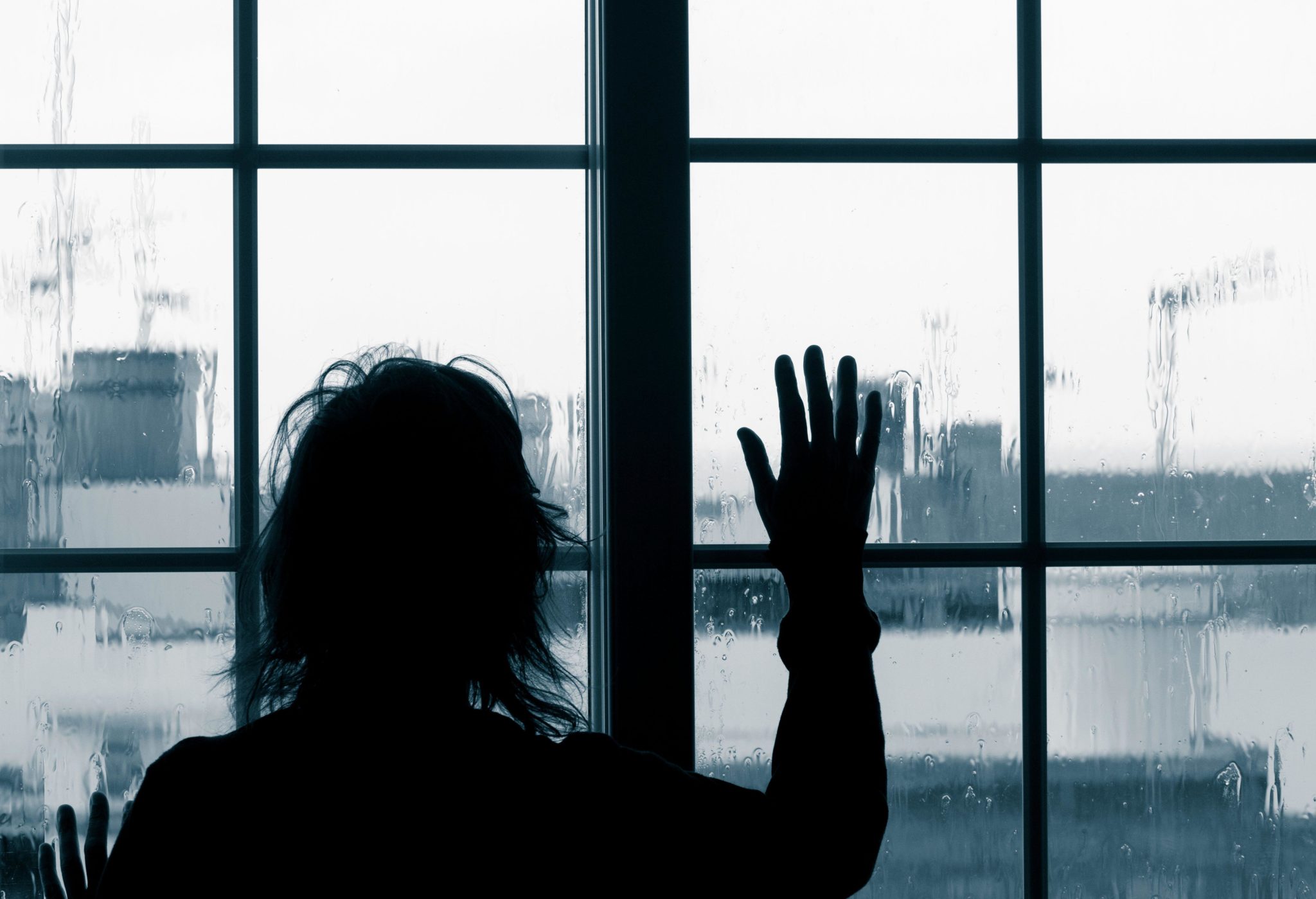 Woman looking out of window on rainy day. Image: Islandstock / Alamy Stock Photo