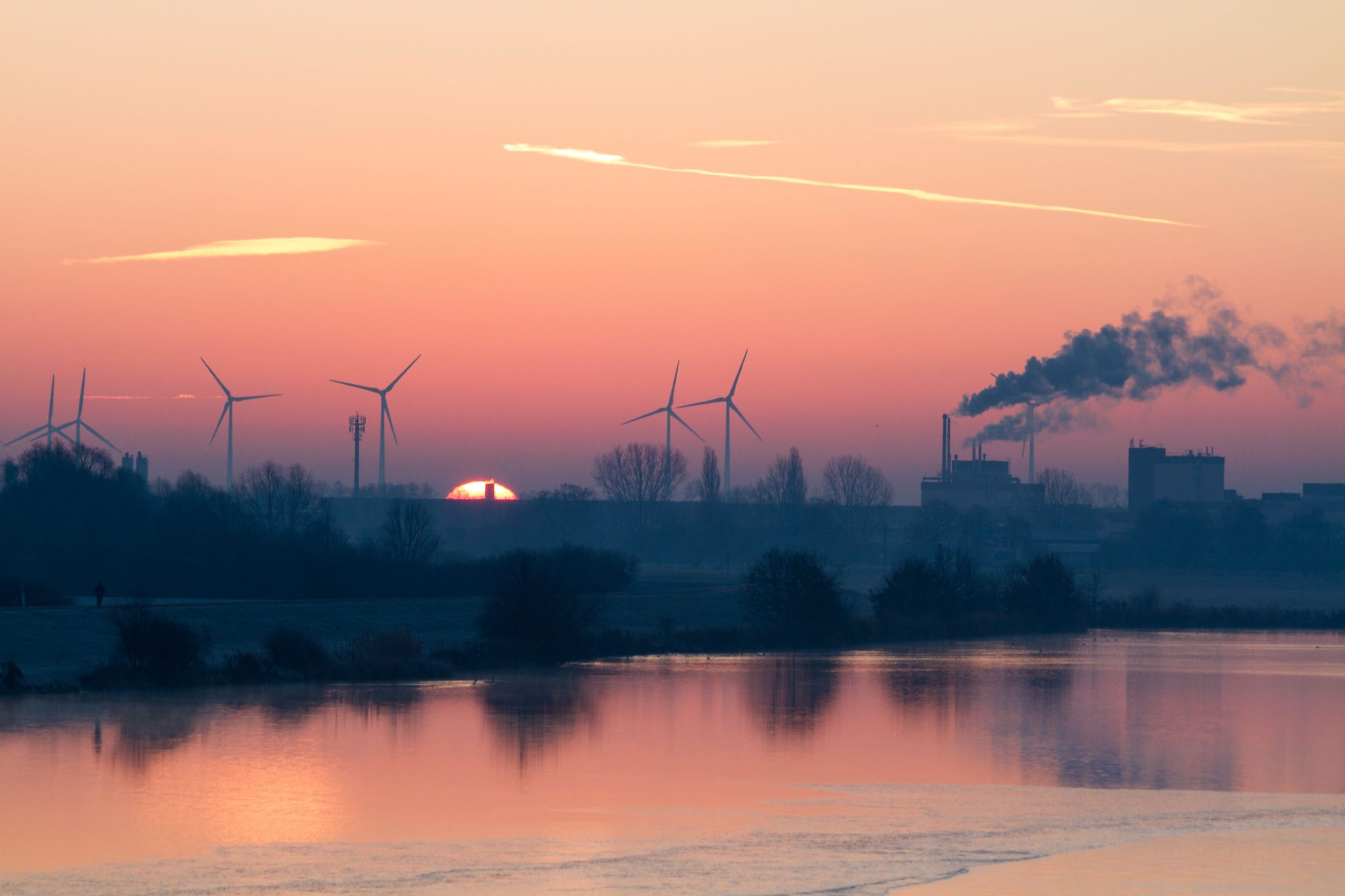 Sunrise behind wind turbines and a smoke stack with in Bremen, Germany in January 2019.