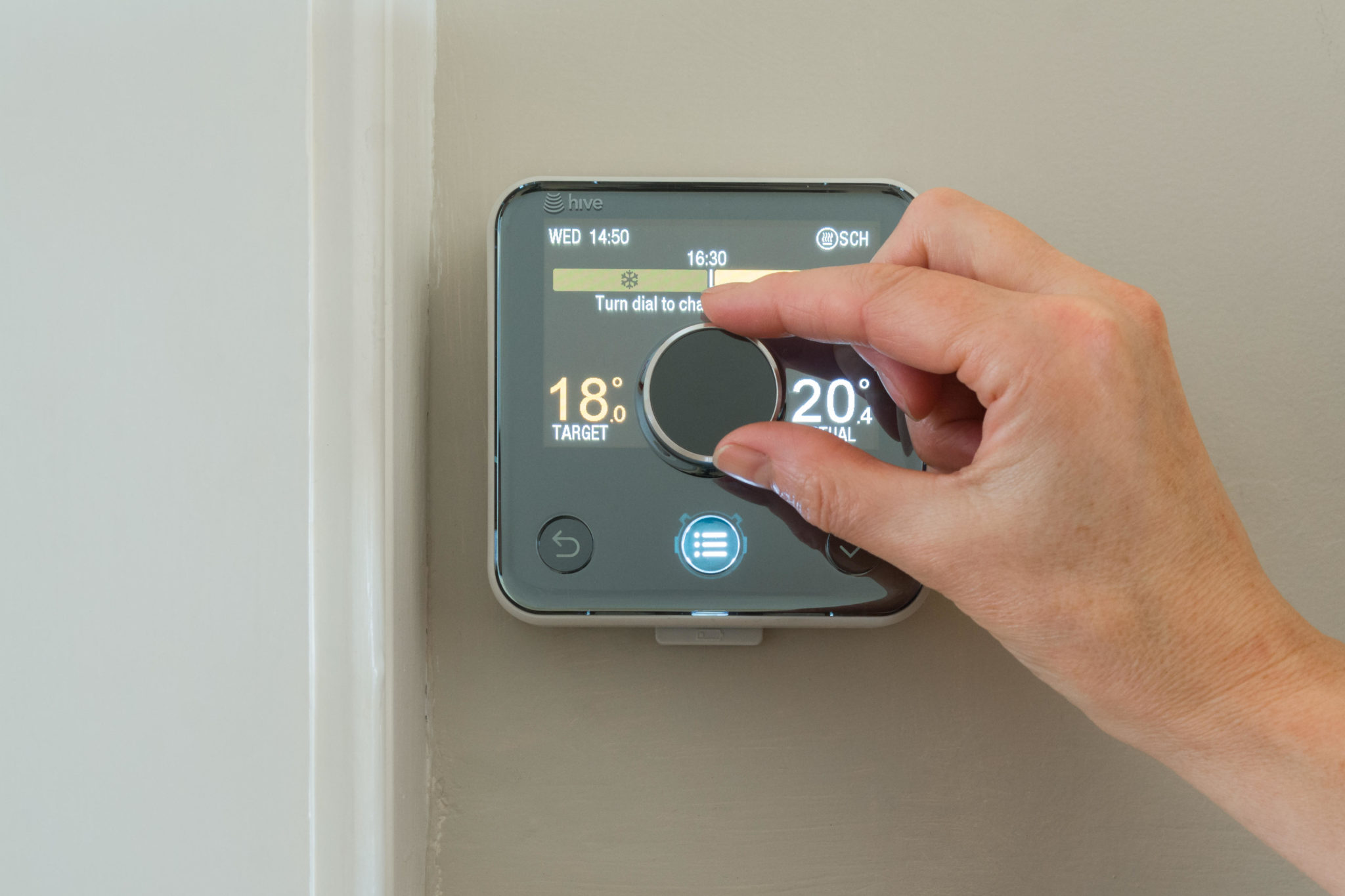 A heating thermostat being turned down by hand in April 2017.