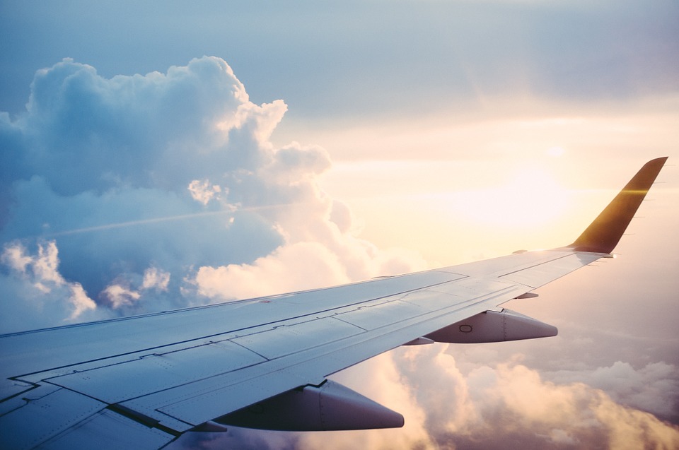 flights. (Image shows the wing of a plane with clouds in the background)