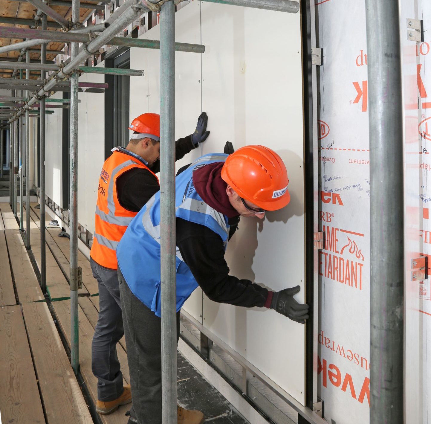 Workmen fix fire-resistant cladding panels and extra thermal insulation to an exterior wall in October 2018