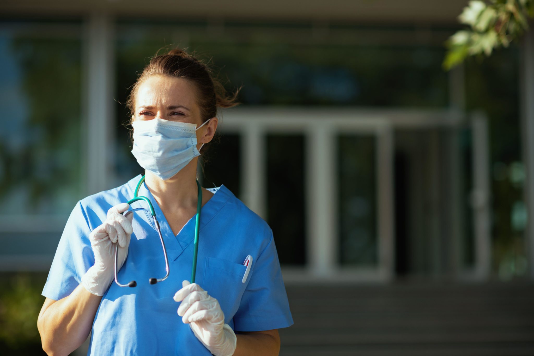 A physician in uniform with a stethoscope is seen near a hospital.