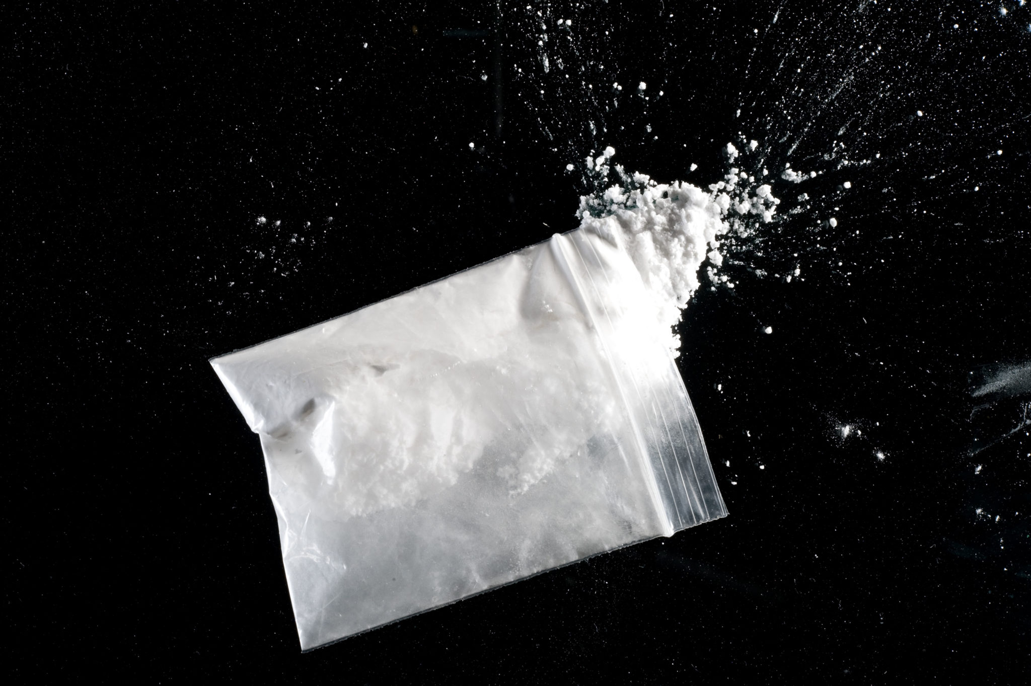 Bag of cocaine powder spilling out onto black surface. Image: Paul Bock / Alamy Stock Photo