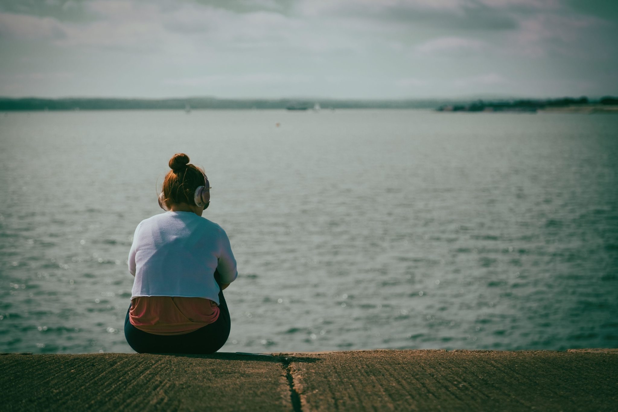 A teenage girl sitting alone near the sea.