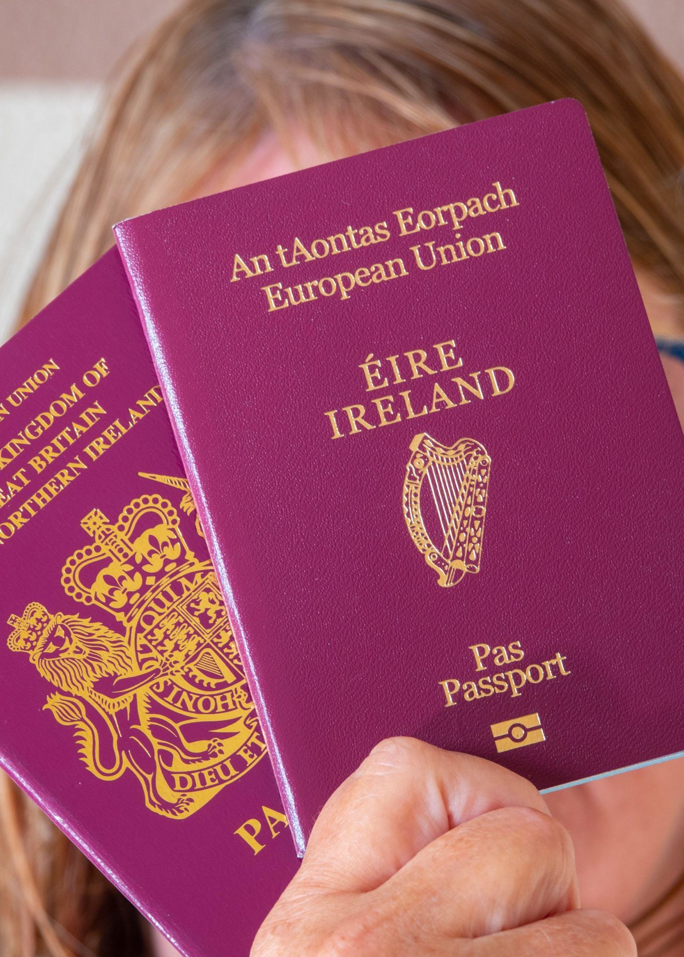 A woman holds an Irish and British passport in front of her face.