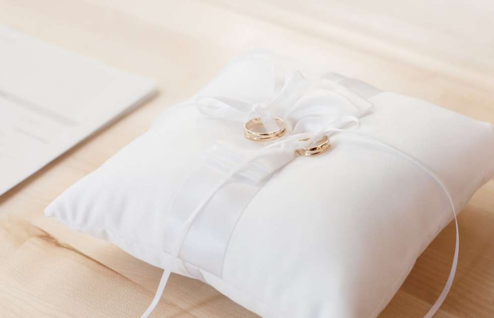 weddings. Image shows two gold wedding rings on a white square cushion.