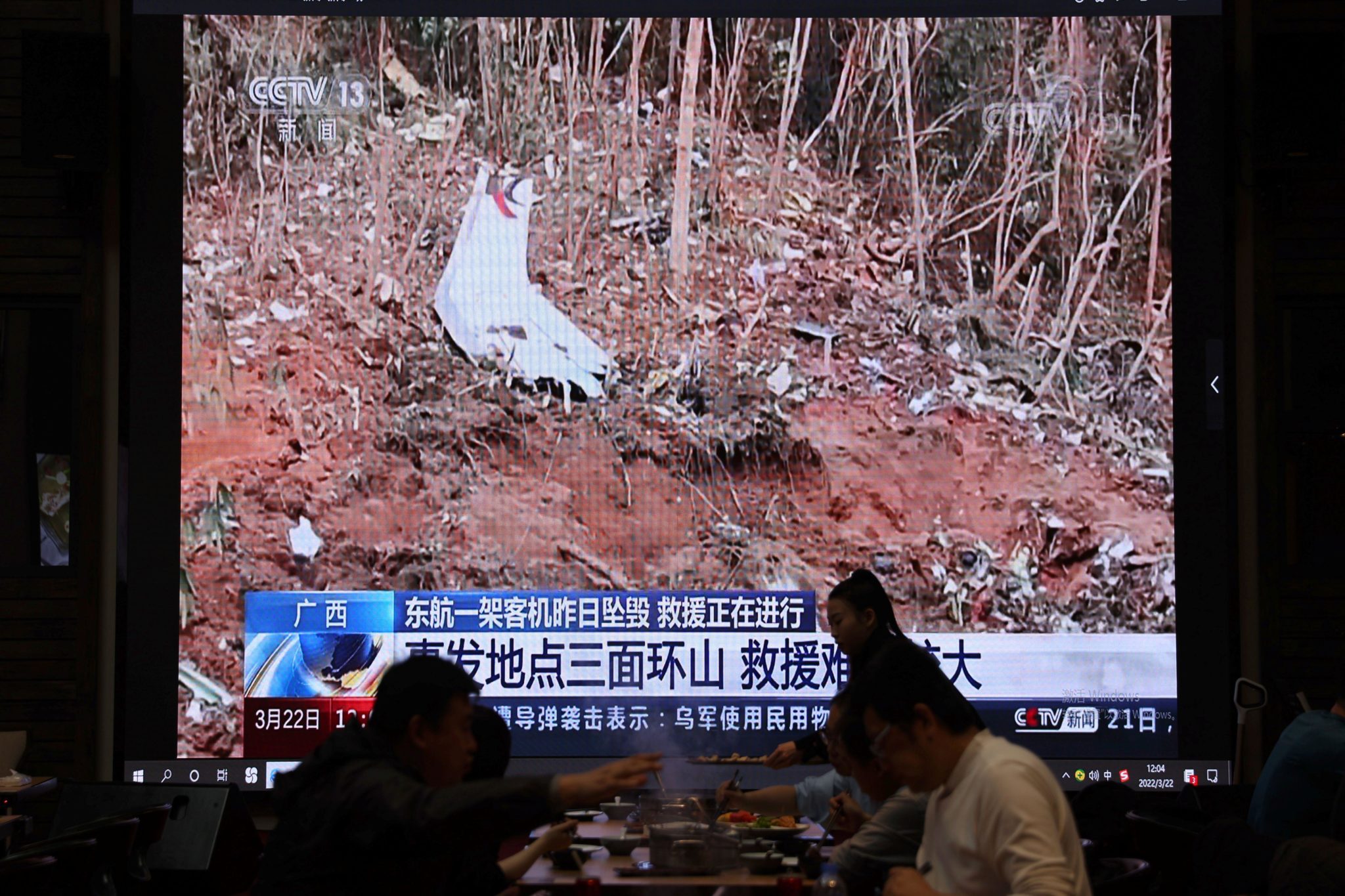 A screen shows news footage of plane debris at the crash site. Image: Cynthia Lee / Alamy Stock Photo