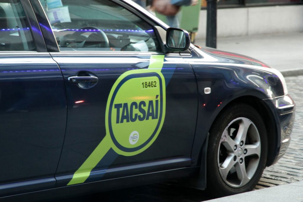 taxi. Image shows dark coloured car with a Tacsaí sign on the driver's door.