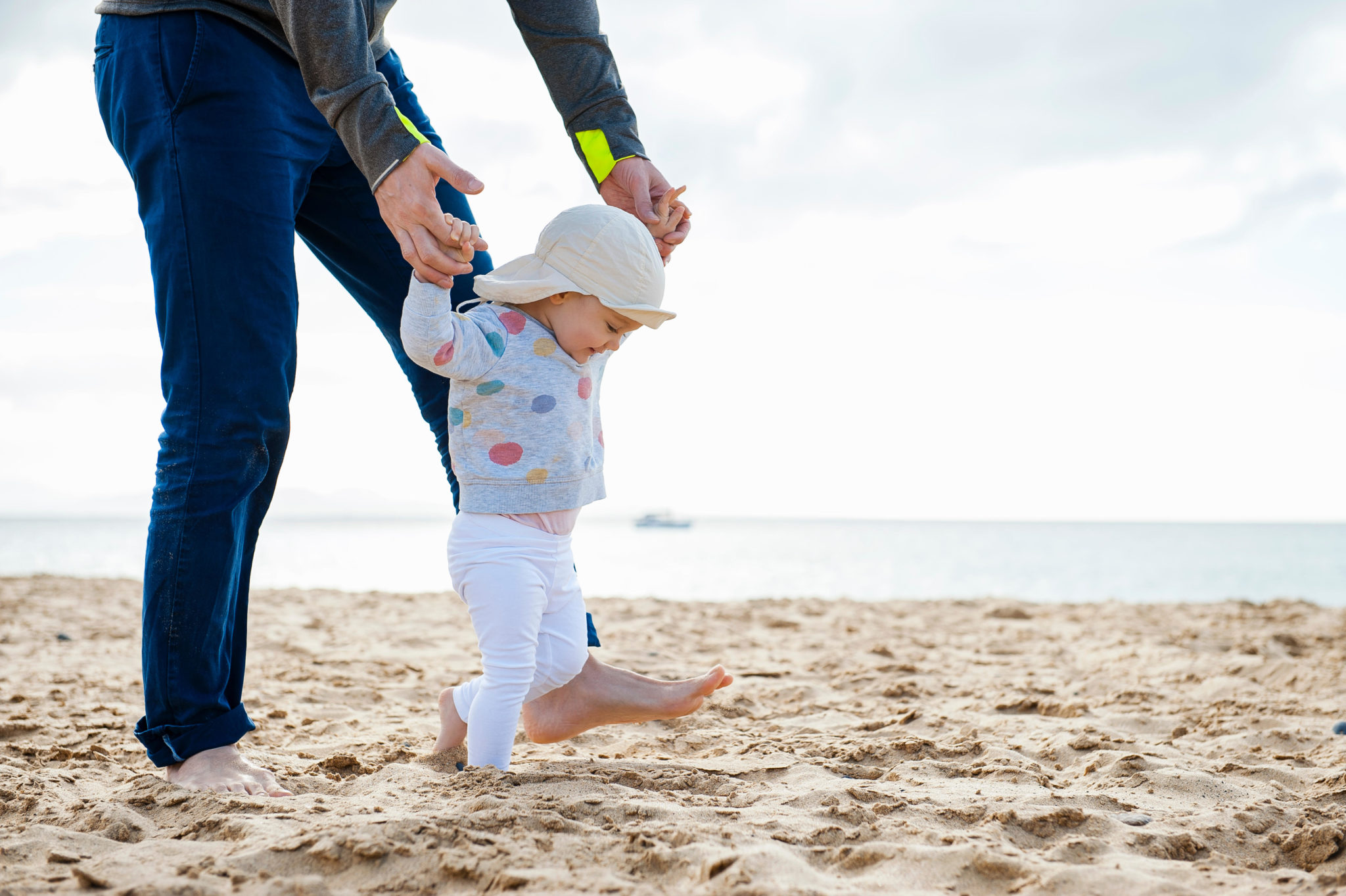 A baby girl walking on the beach with the help of her father. Image: Westend61 GmbH / Alamy Stock Photo