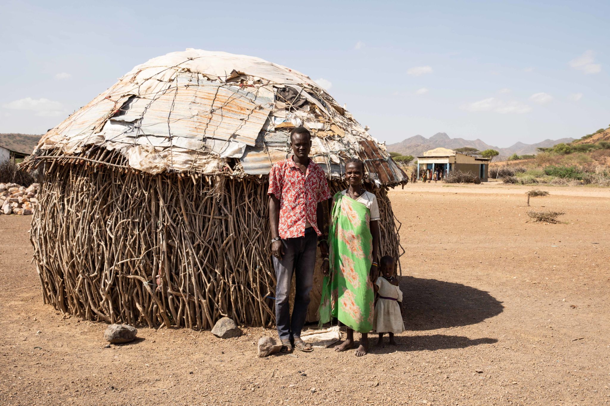 Ereng Kaleng Kalimapus poses for a photo with his wife and child outside their bedroom in Milimatatu Village, Kaeris, Turkana County in Northern Kenya, 27-06-22. Image: Lisa Murray/Concern Worldwide.