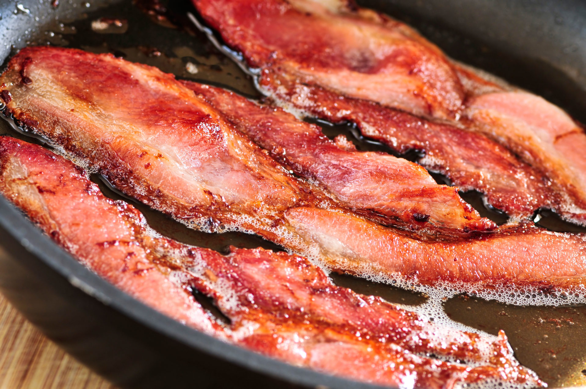 Bacon strips sizzling on a frying pan.