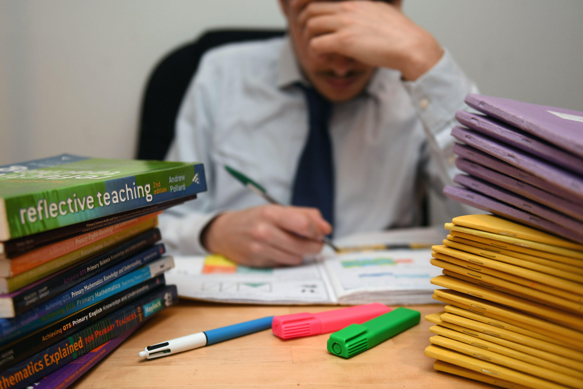 A school teacher next to piles of classroom books.