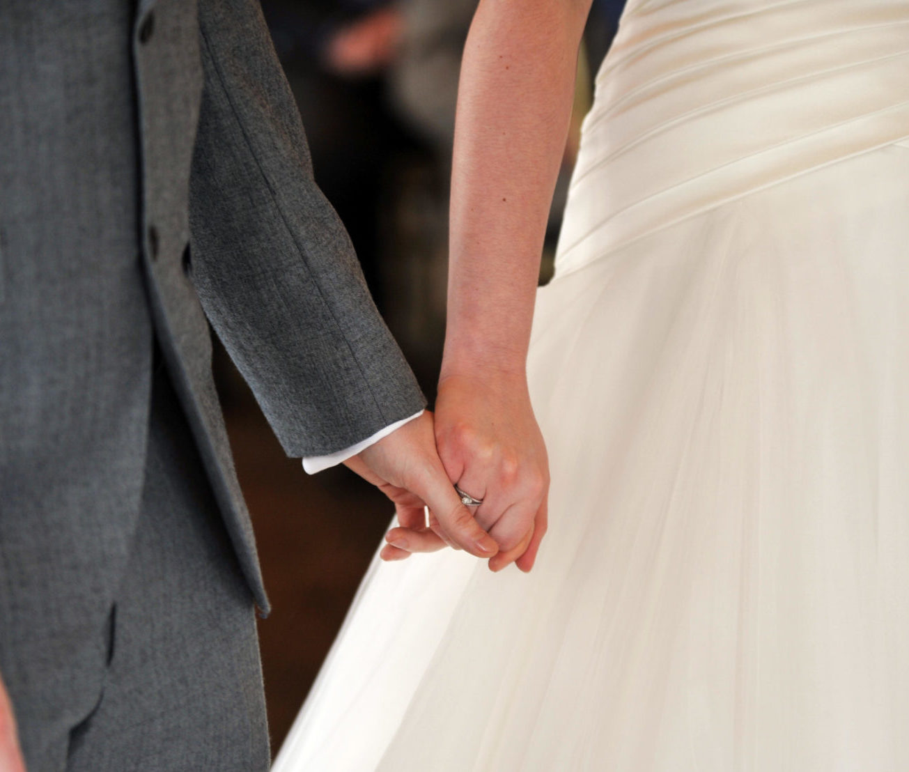 Close up of a bride and groom holding hands during a marriage ceremony.