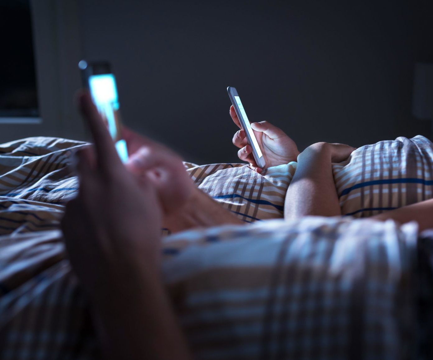 A couple ignoring each other lying in bed at night while using mobile phones