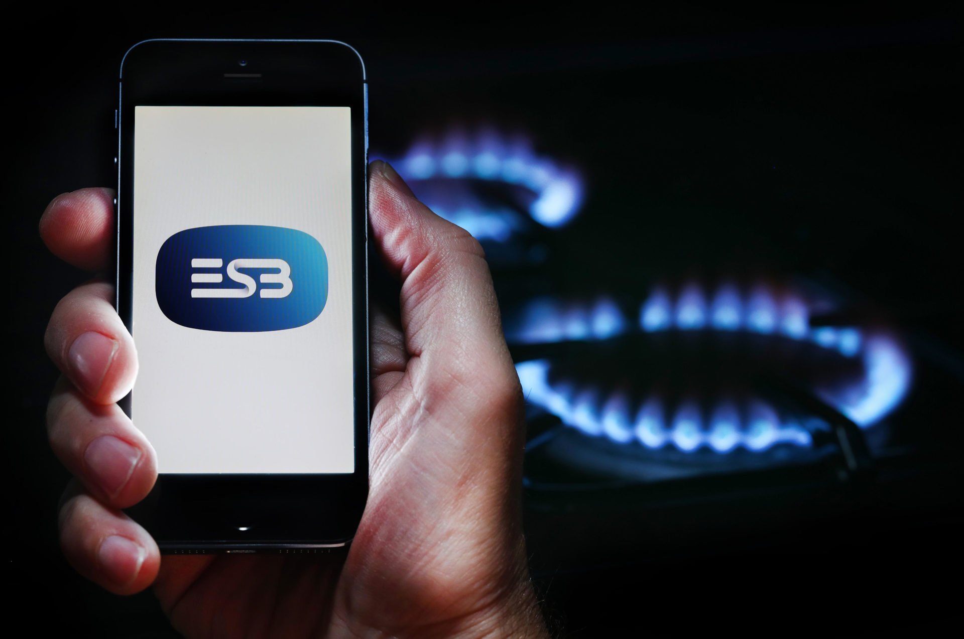 A man looking at the website logo for energy company ESB on his phone in front of his gas cooker.
