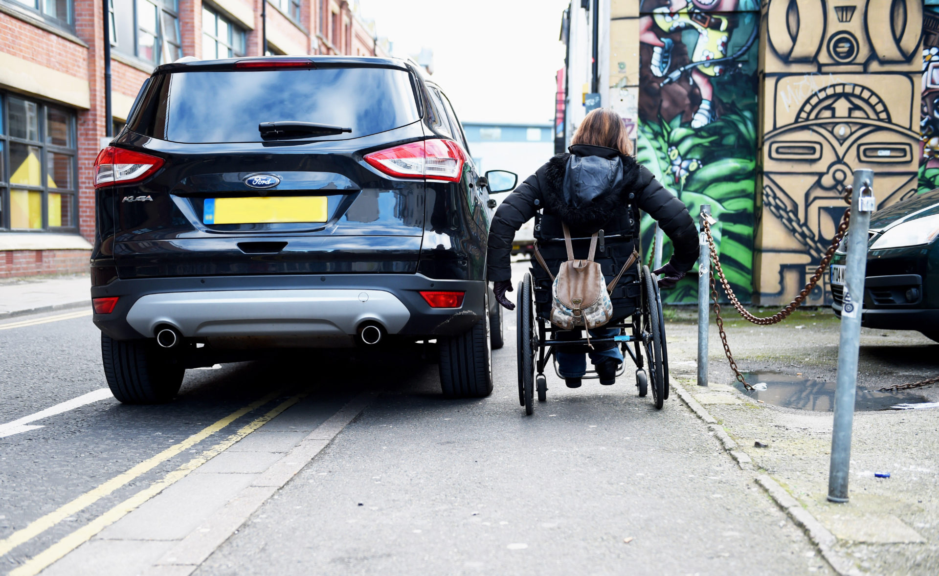 Wheelchair user struggles to pass by badly parked car on pavement and double yellow lines in Brighton UK, 11-02-2016.