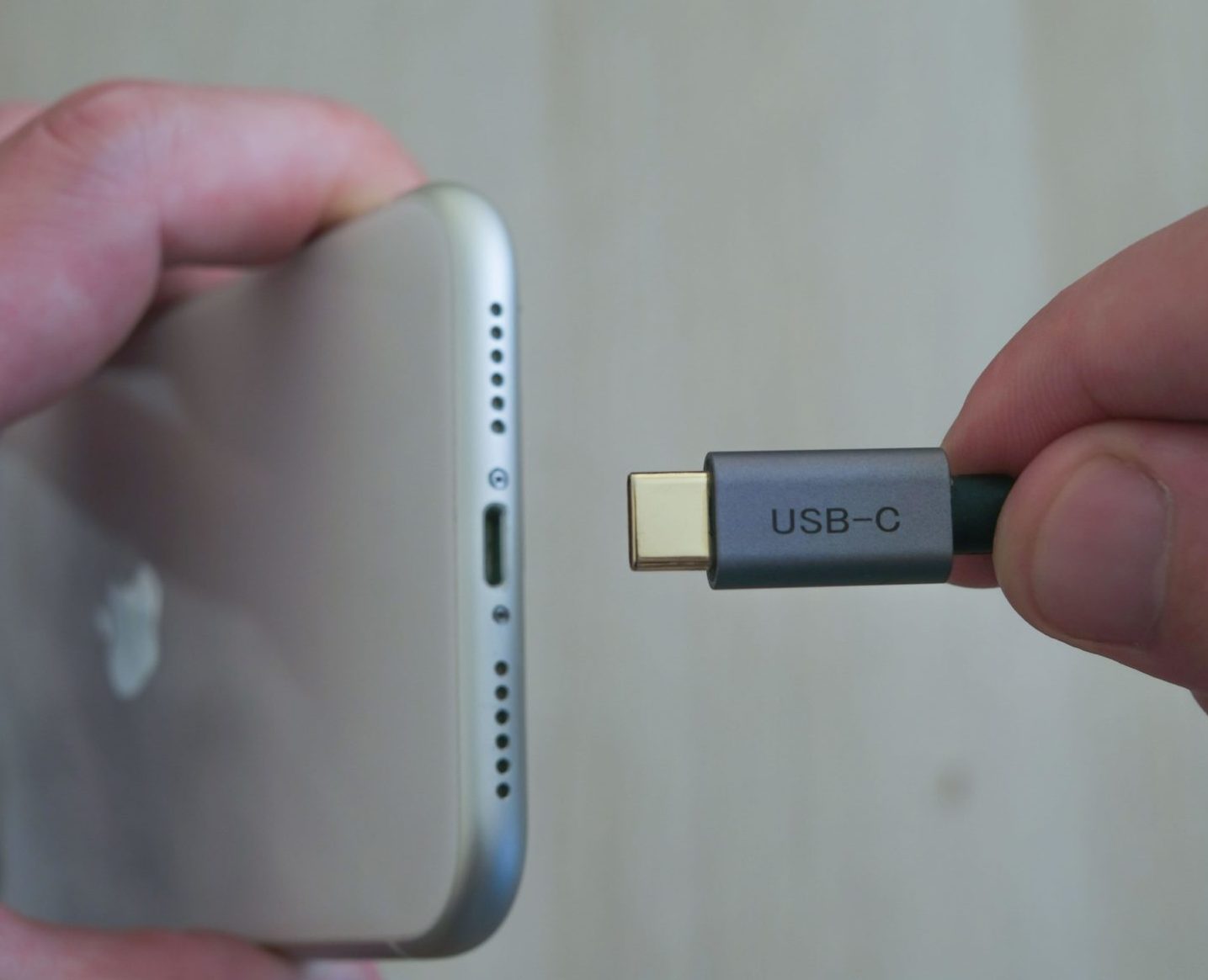 A person holds an Apple iPhone and a USB-C cable