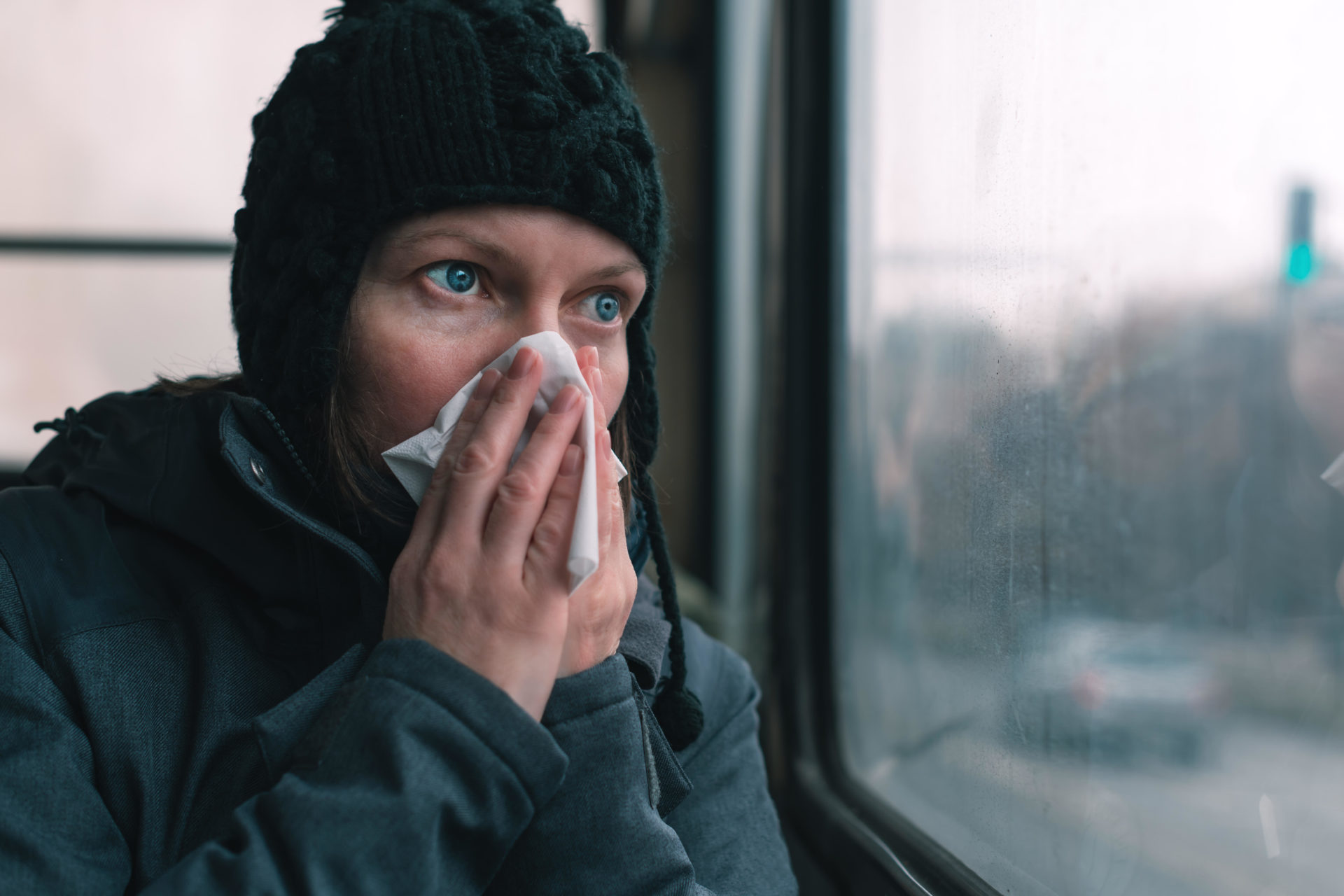 Woman blowing her nose into paper handkerchief on the bus on a cold winter day.