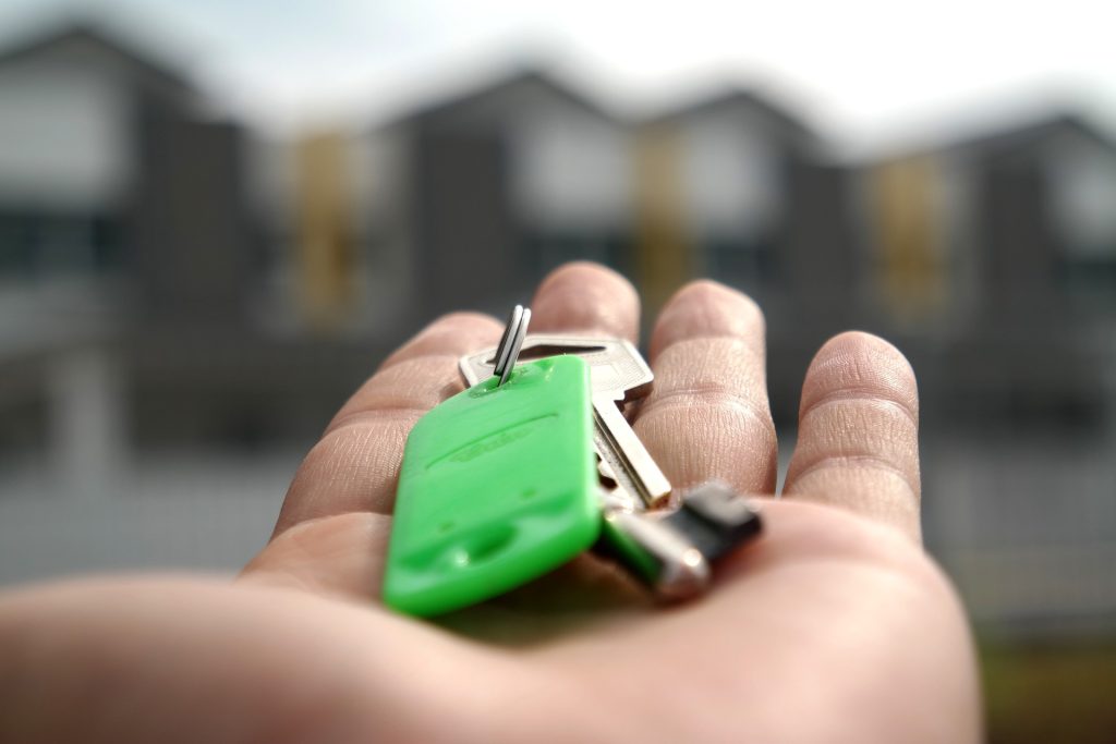 mortgage rules. Image shows an outstretched hand holding a set of keys with a bright green keyring on them.