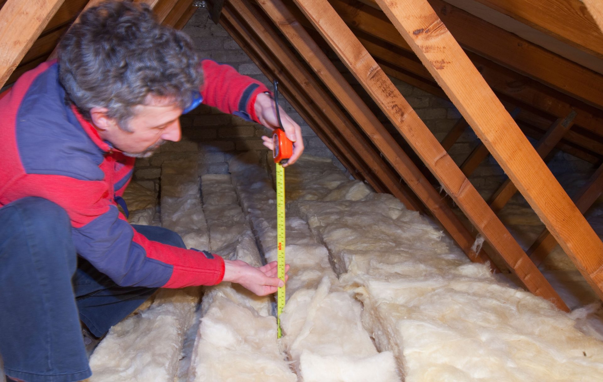 A man measures loft insulation to cut down heat loss in a house.