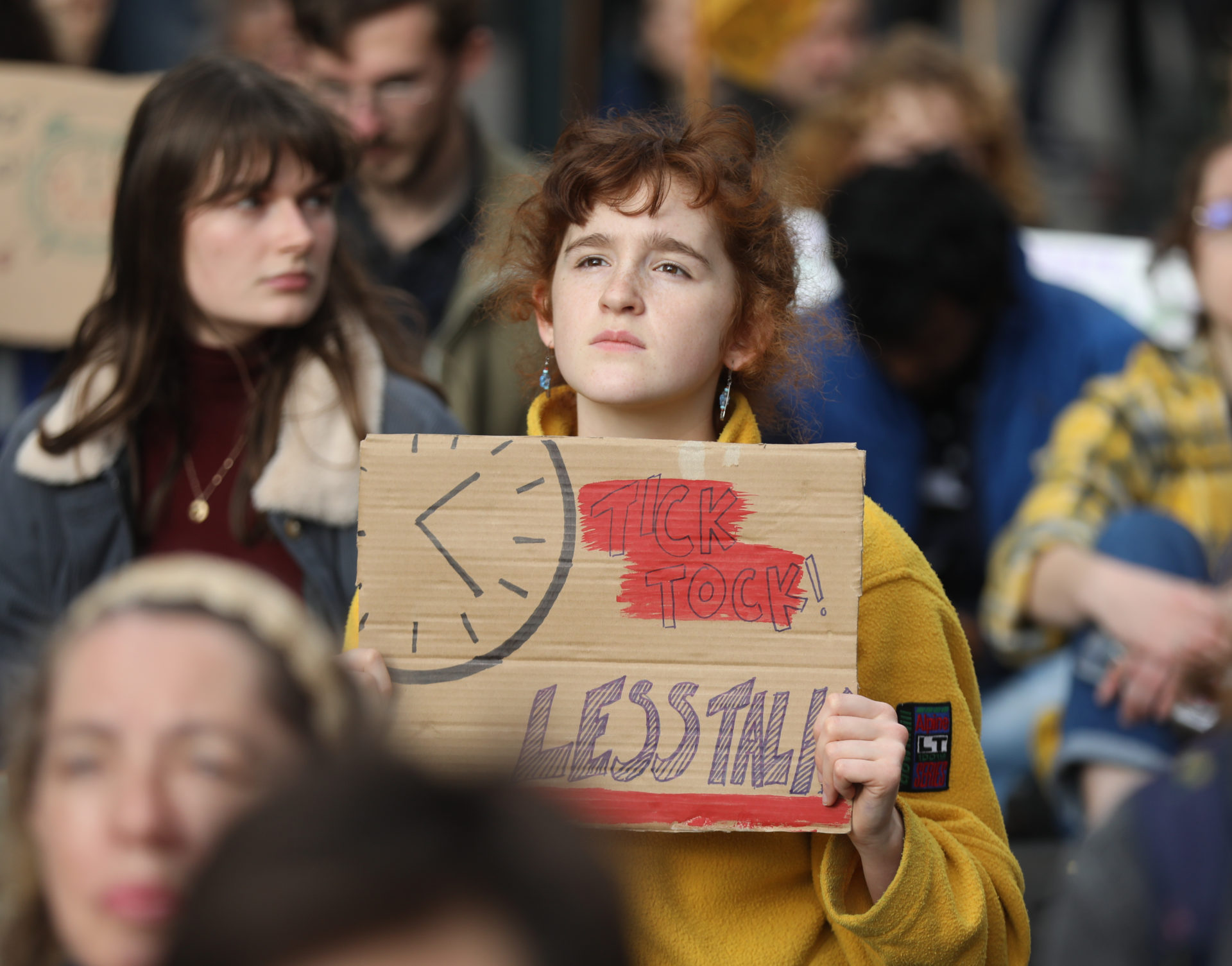 TCD Drama and Theatre Studies student Martha Cosgrove holding a sign saying "Tick Tock Less Talk" outside Dáil Eireann, 11-11-22. Image: Leah Farrell/RollingNews