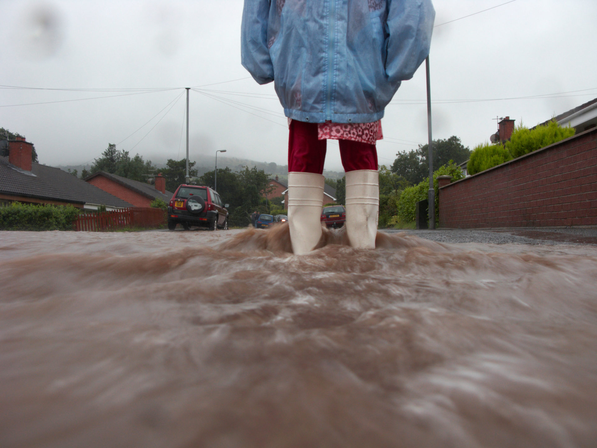 Young girl wearing raincoat and wellington boots standing in water from rain and river overflow flooding a street in Newtownabbey. Image: Radharc Images / Alamy