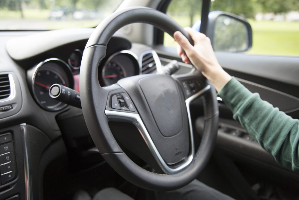 dangerous. Image shows a right hand holding onto a car steering wheel.