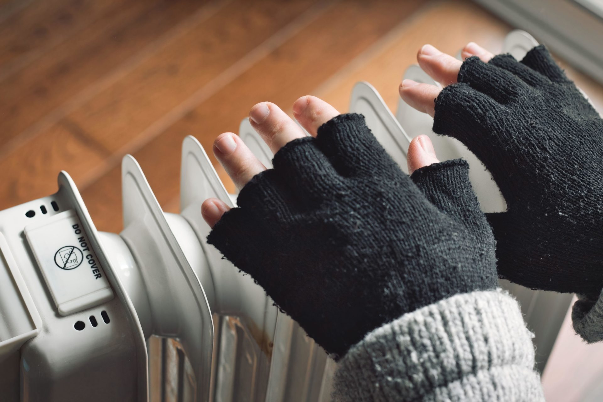 A person wearing black woolly fingerless gloves close to a domestic radiator. Image: Tennessee Witney / Alamy
