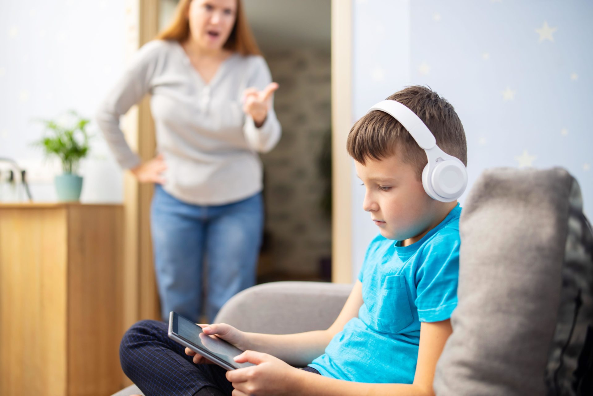 Boy using tablet with headphones ignores his mom. 