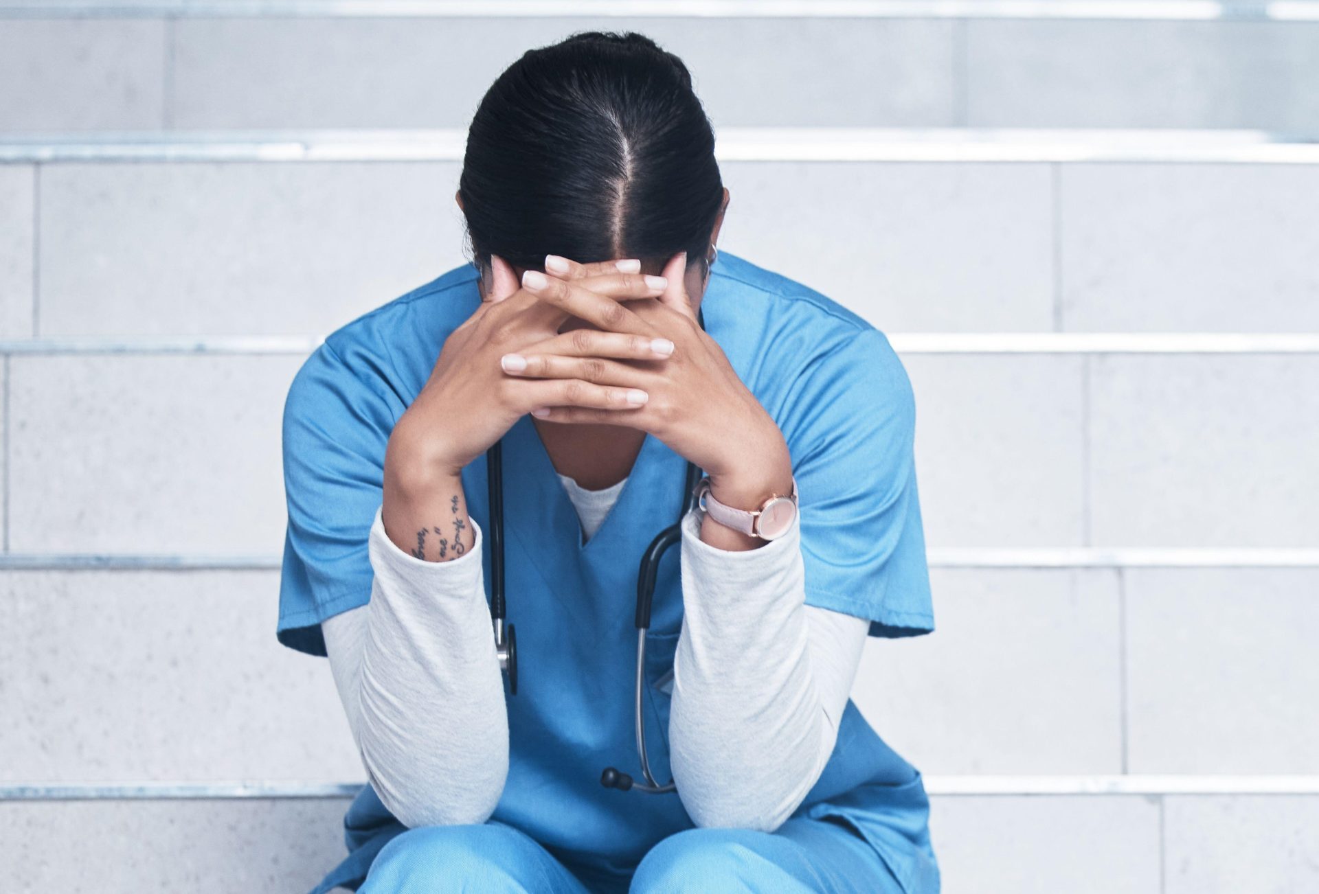 A nurse looking stressed while sitting on a staircase.