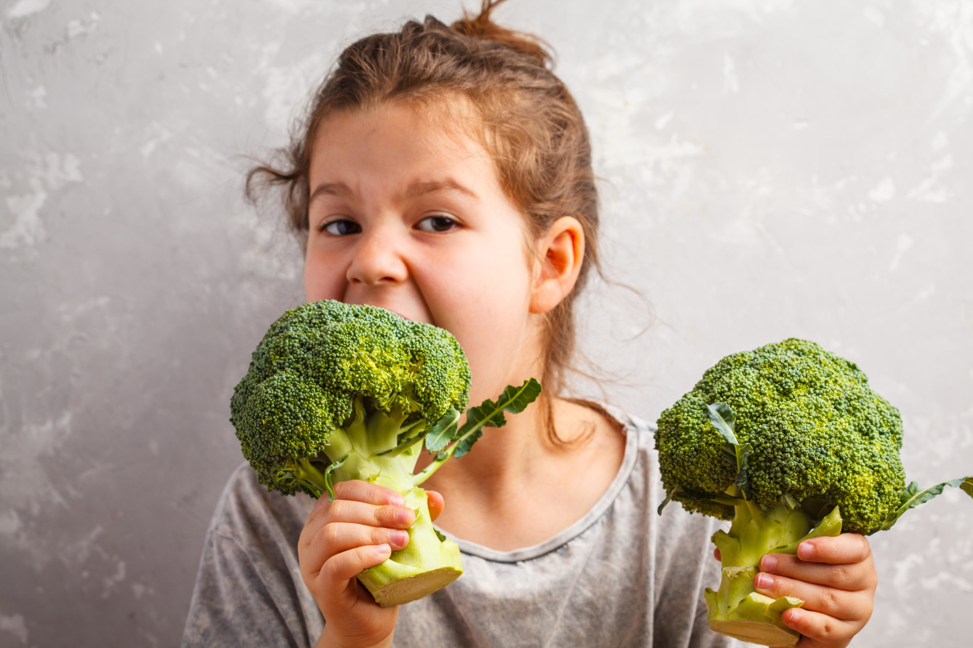 A young girl eating broccoli. 