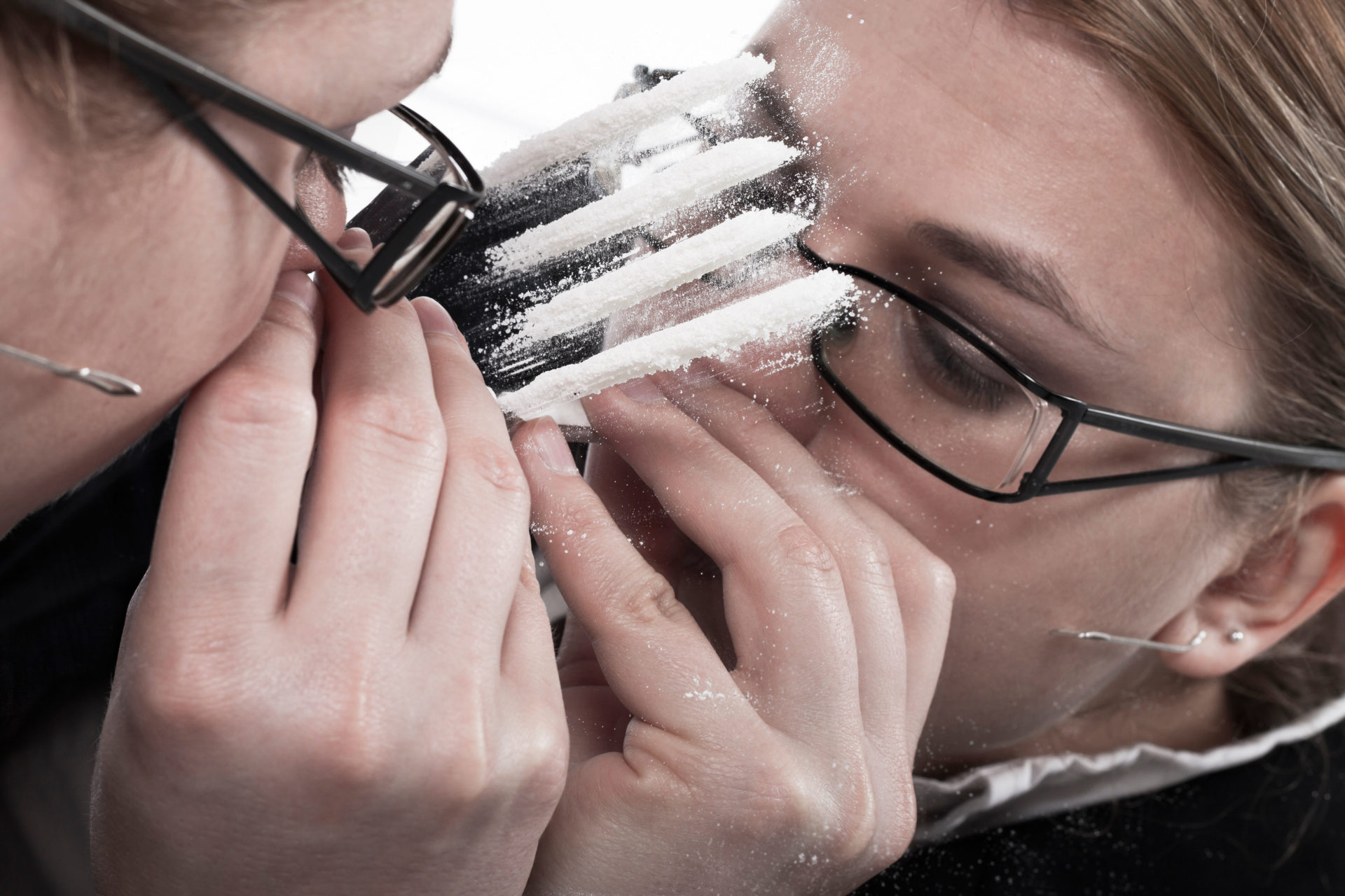 Woman reflected in mirror snorting line of cocaine.