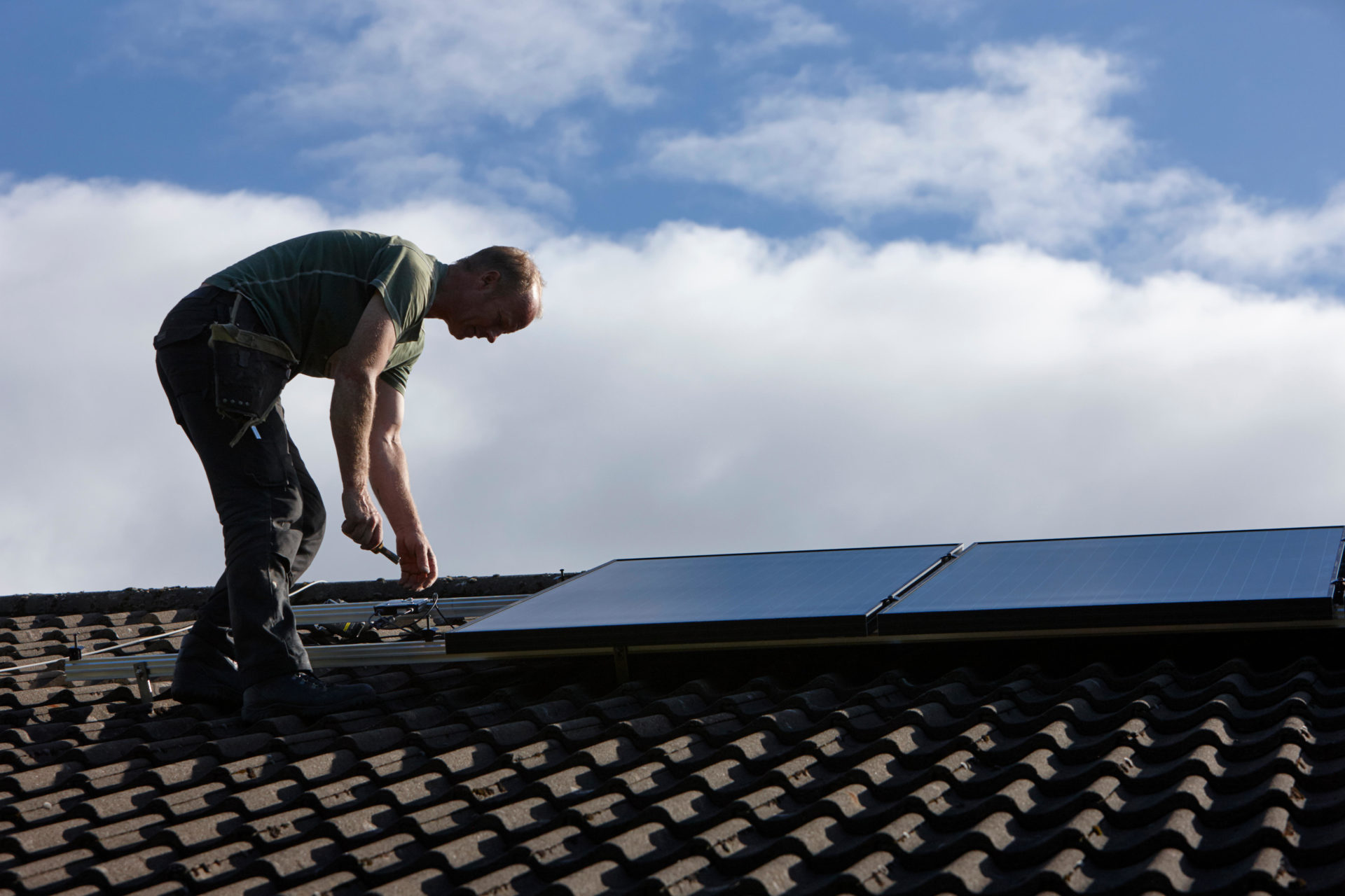 A man installing a rooftop solar panel array.