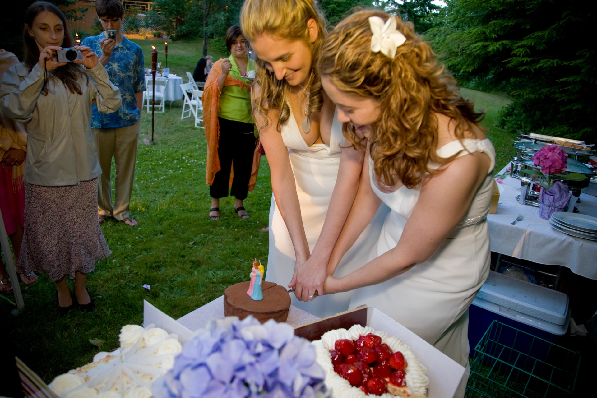 A couple cuts the wedding cake at the lesbian wedding reception while guests watch