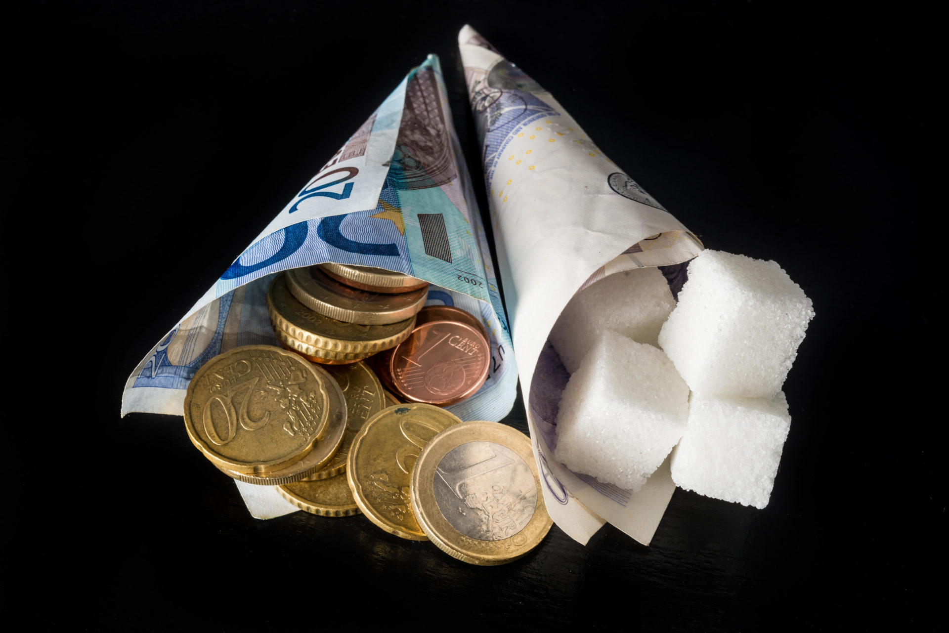 Paper cones with sugar cubes in one and money (euro and pound notes and euro cents coins) symbolising sugar tax in EU
