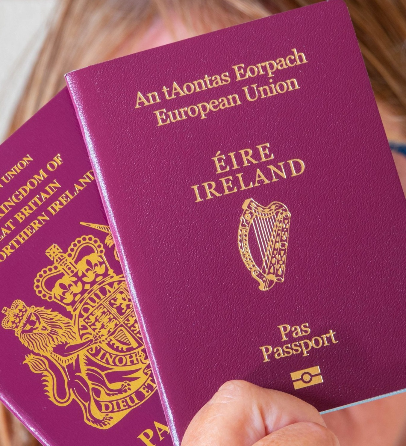A woman holds an Irish and British passport in front of her face