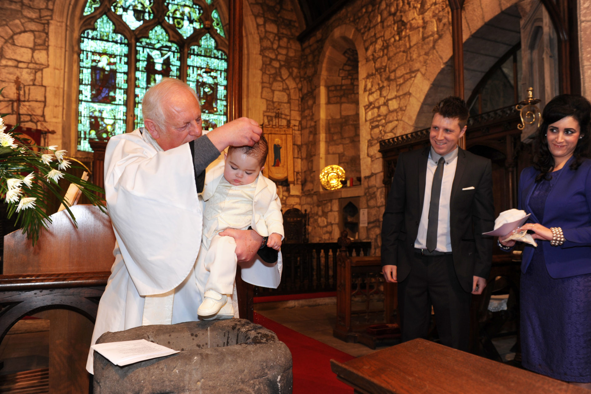 Young child being christened by a vicar and watched by the parents England Uk. Britain England christening children church family service baptism