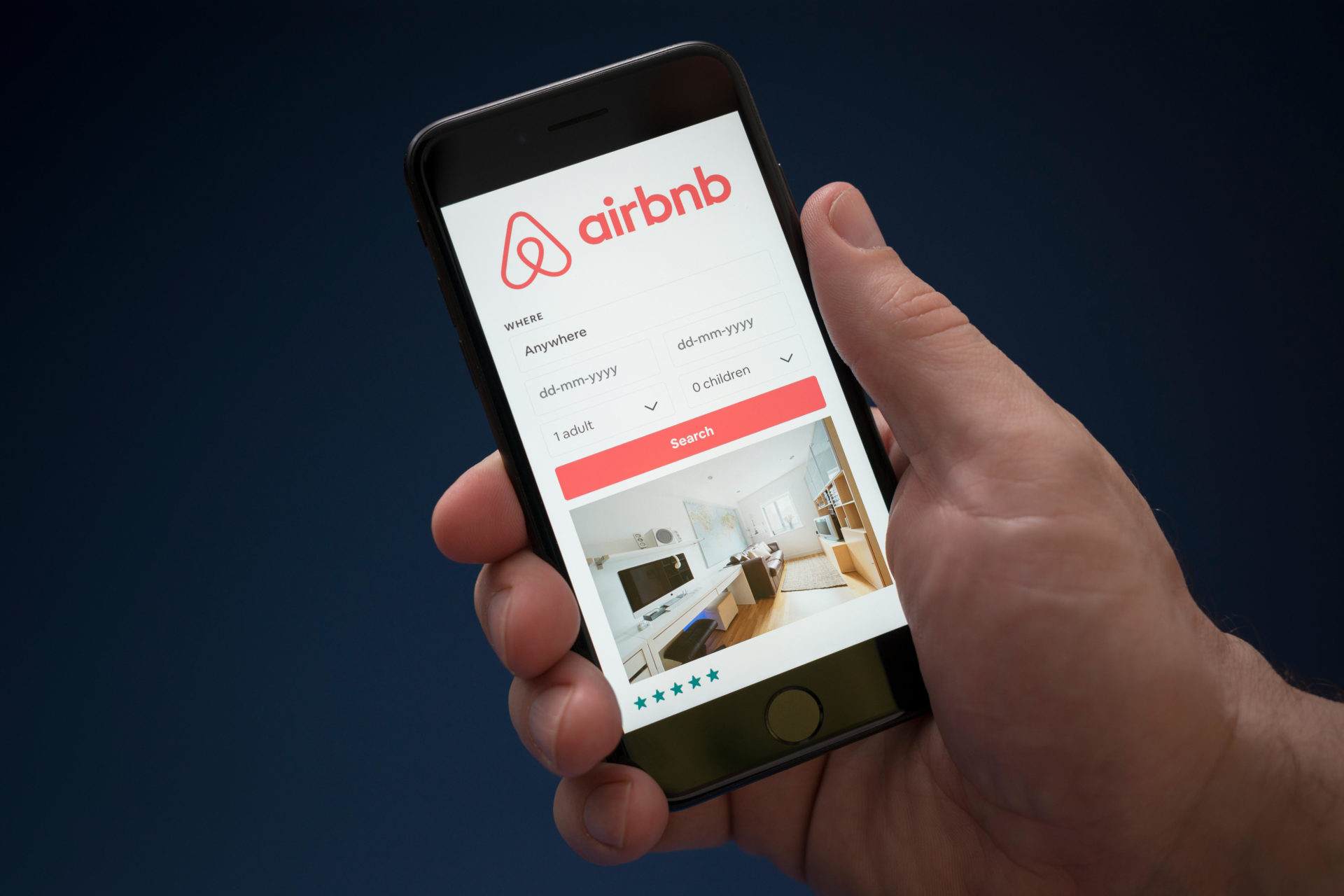 A man looks at his phone which displays the Airbnb logo