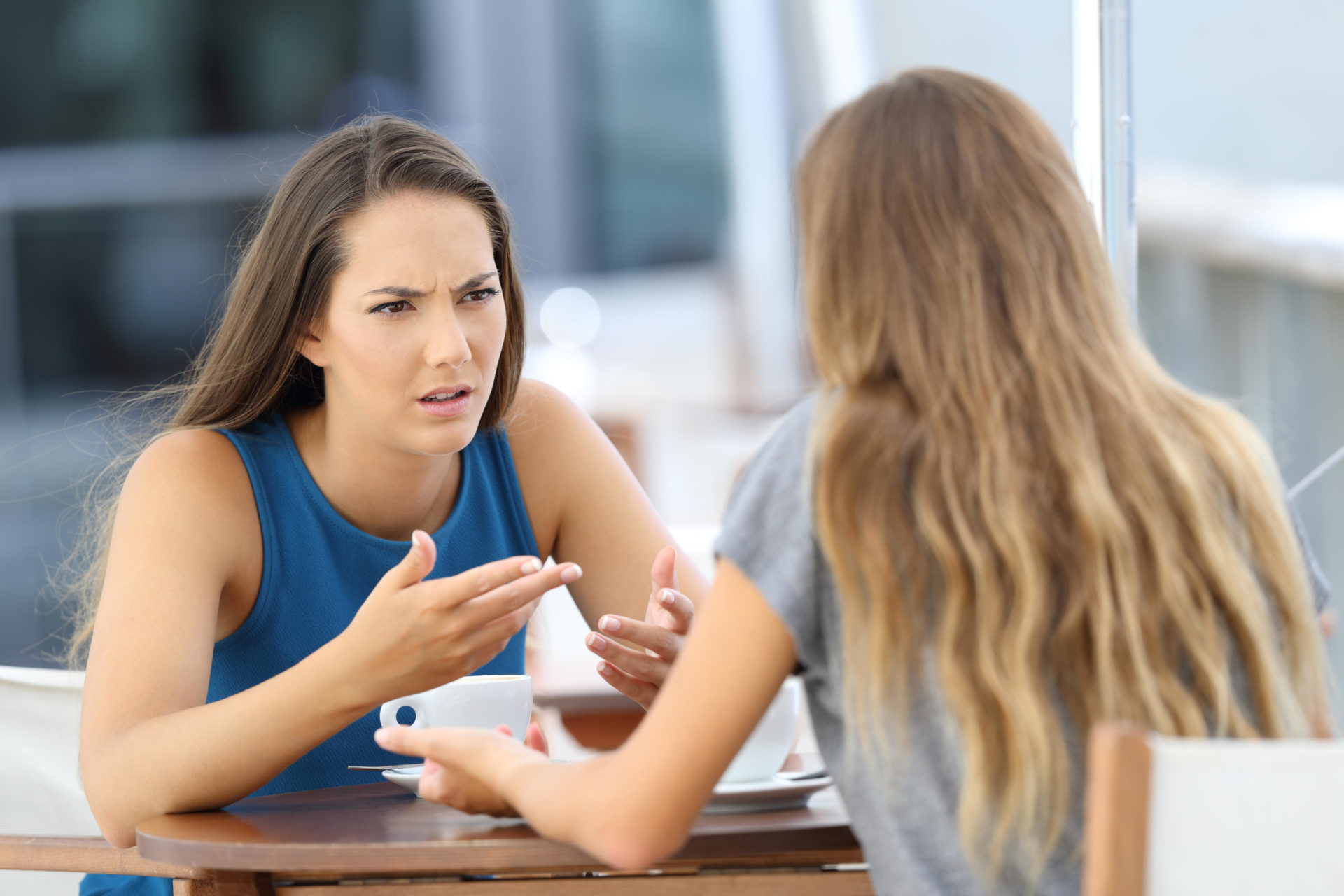 K3YBH3 Two angry girls talking seriously sitting in a coffee shop